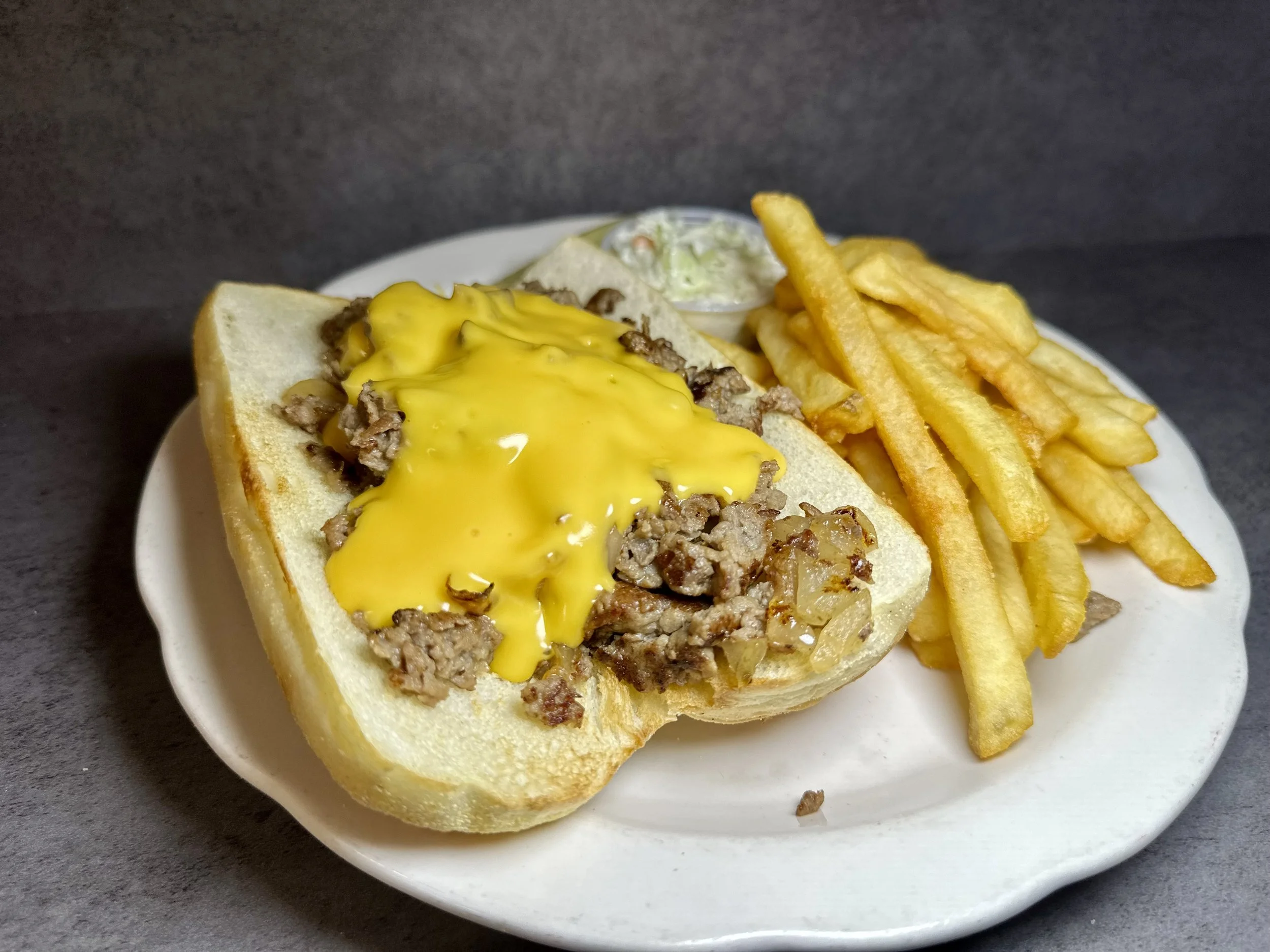 Beef and gravy on a split bread roll with fries and a small container of coleslaw on a white plate.
