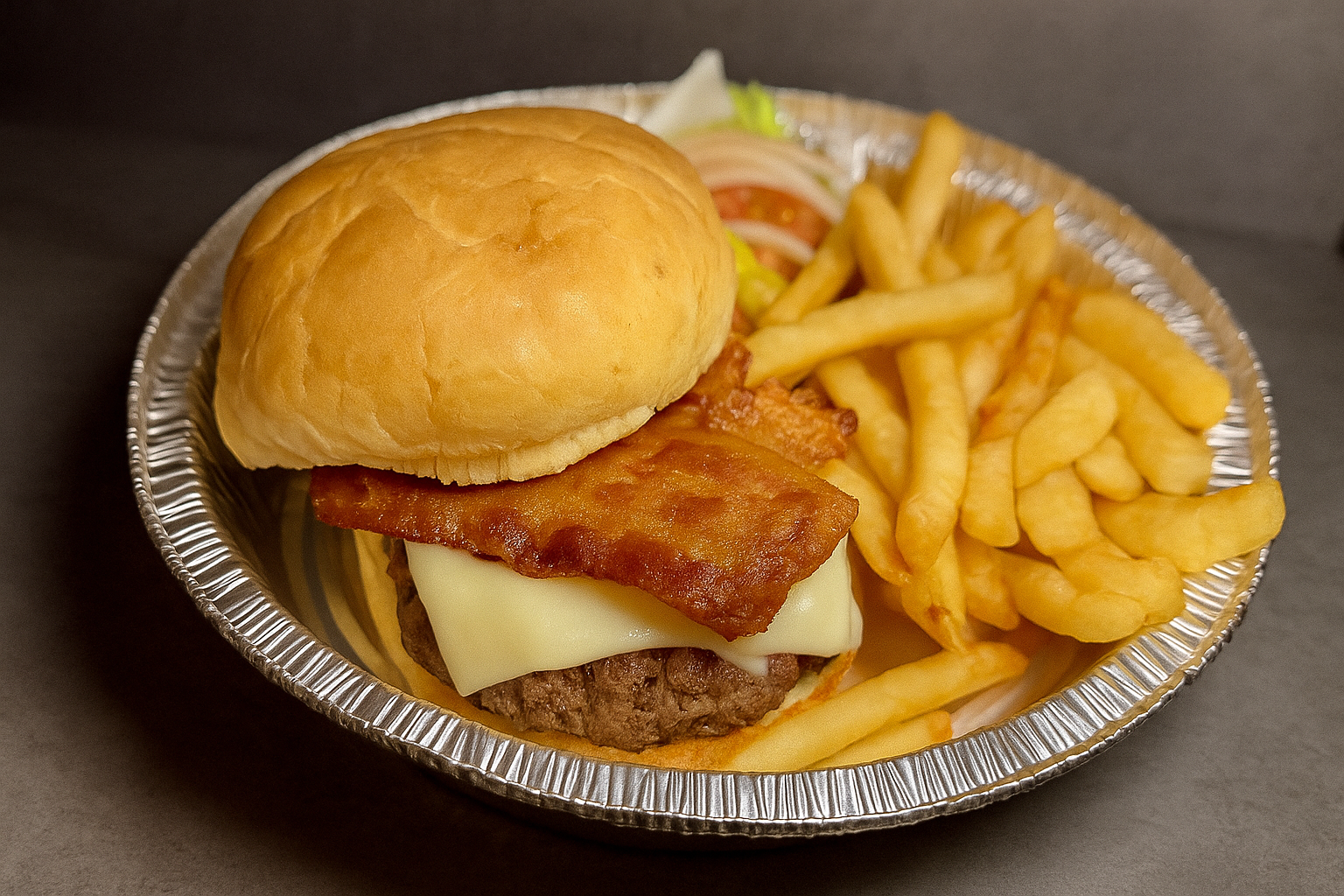 A hamburger with bacon, cheese, lettuce, tomato, and a bun, served with French fries in a disposable aluminum tray.