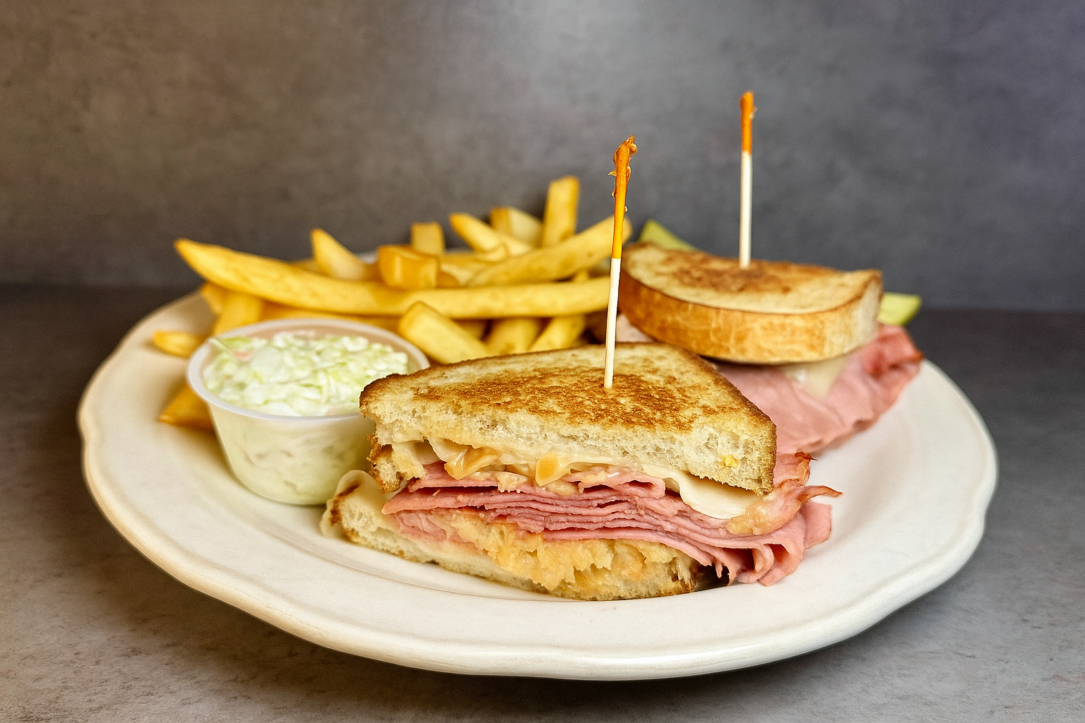 Ham and cheese sandwich with fries and coleslaw on a white plate.