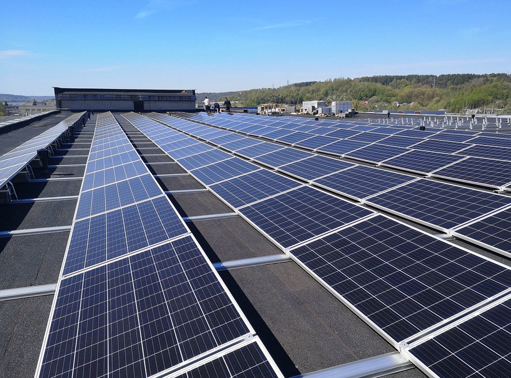 Solar panels installed on the roof of a building with a clear blue sky and distant trees in the background.