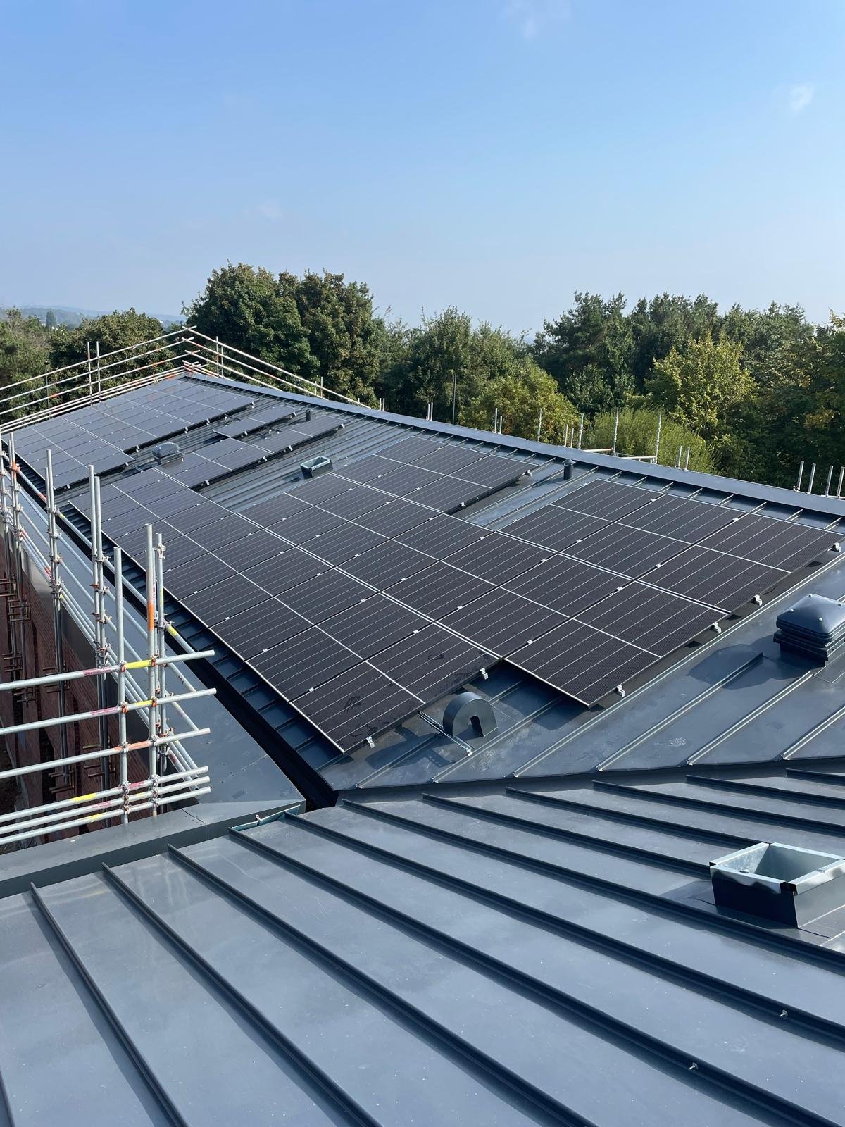 Rooftop with solar panels under a blue sky and green trees in the background.