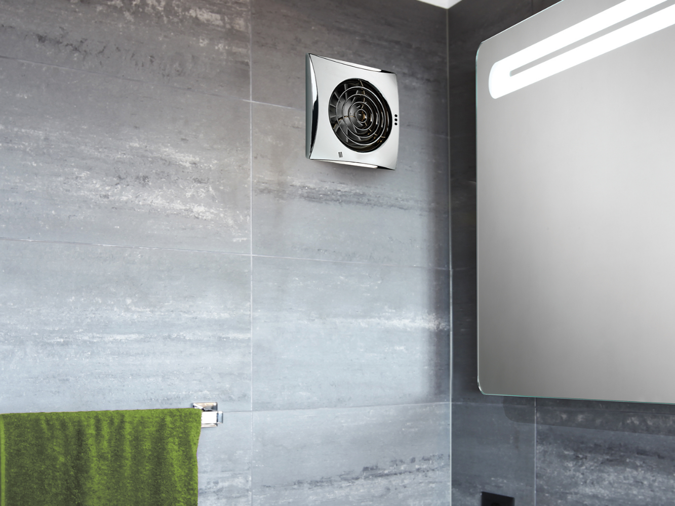 Close-up of a modern bathroom wall with a ventilation fan, part of a mirror, and a green towel hanging on a rail.
