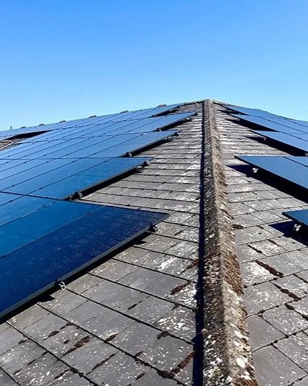 A roof with solar panels installed on one side and traditional shingles on the other, under a clear blue sky.
