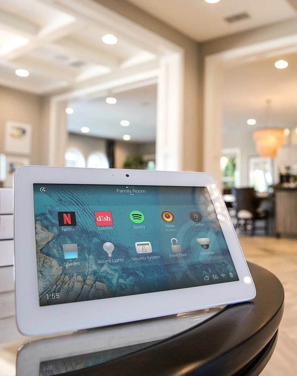 Smart home control panel displaying apps for Netflix, satellite, Spotify, Relax, Shades, Accent Lights, Security System, Front Door, and Cameras in a living room.