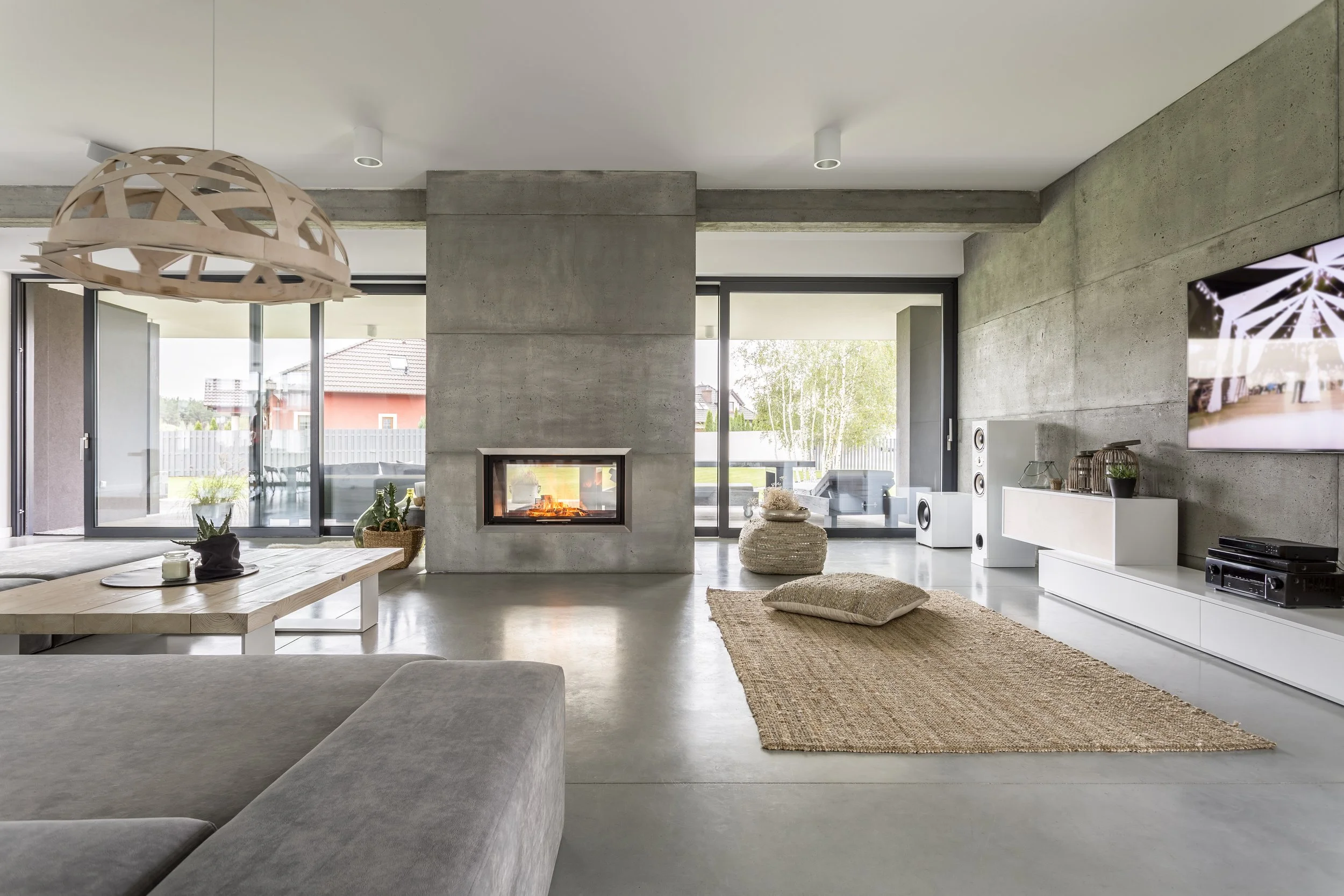 Modern living room with concrete walls, fireplace, large sliding glass doors, and minimalistic decor.