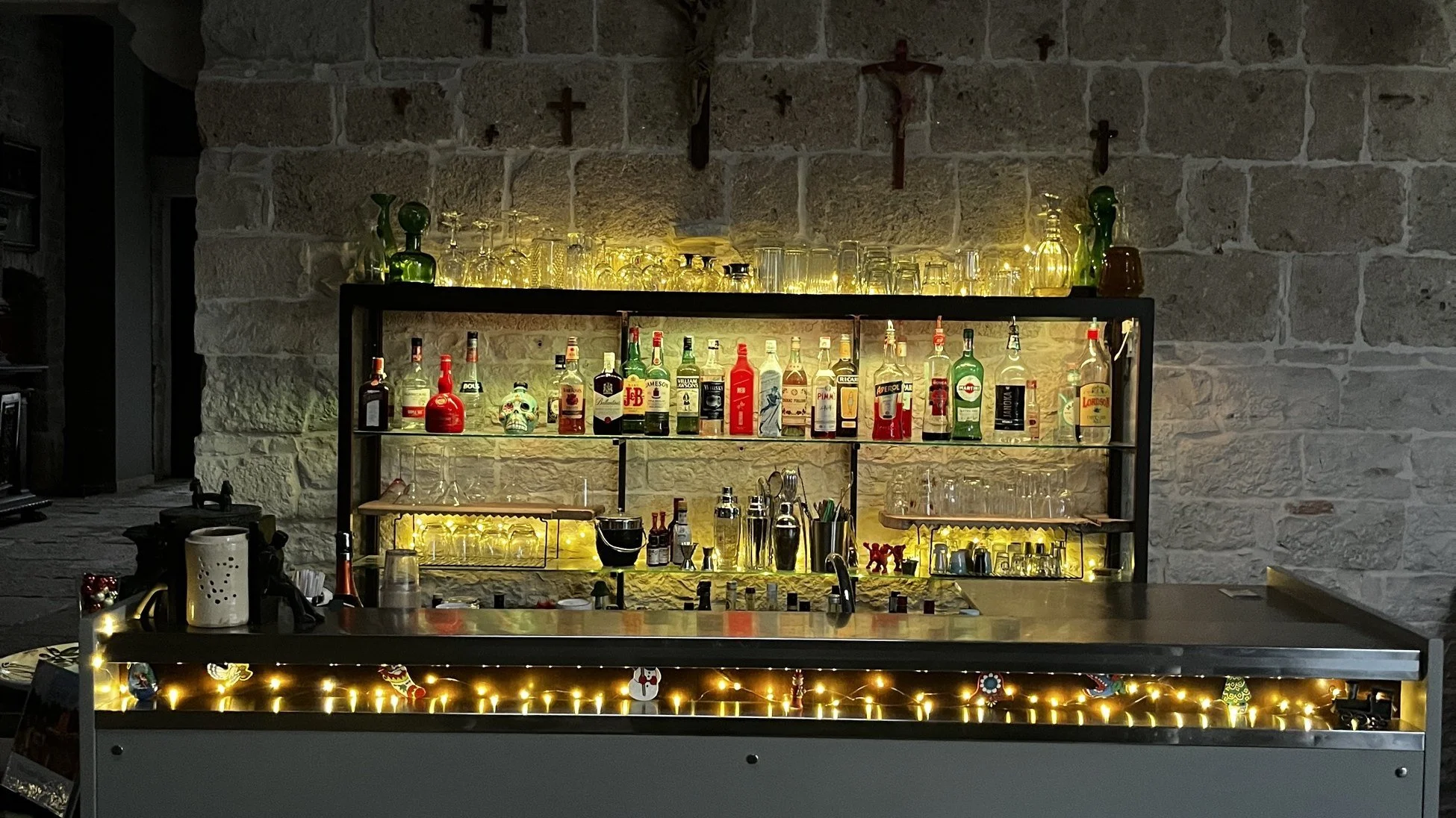 Villa Cappelli bar with bottles lit on shelves against a stone wall
