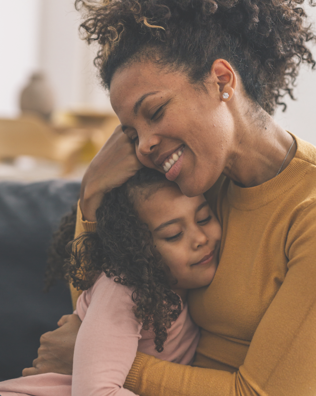 A joyful woman and young girl hugging each other tightly, with the woman smiling and the girl resting her head on the woman's chest.