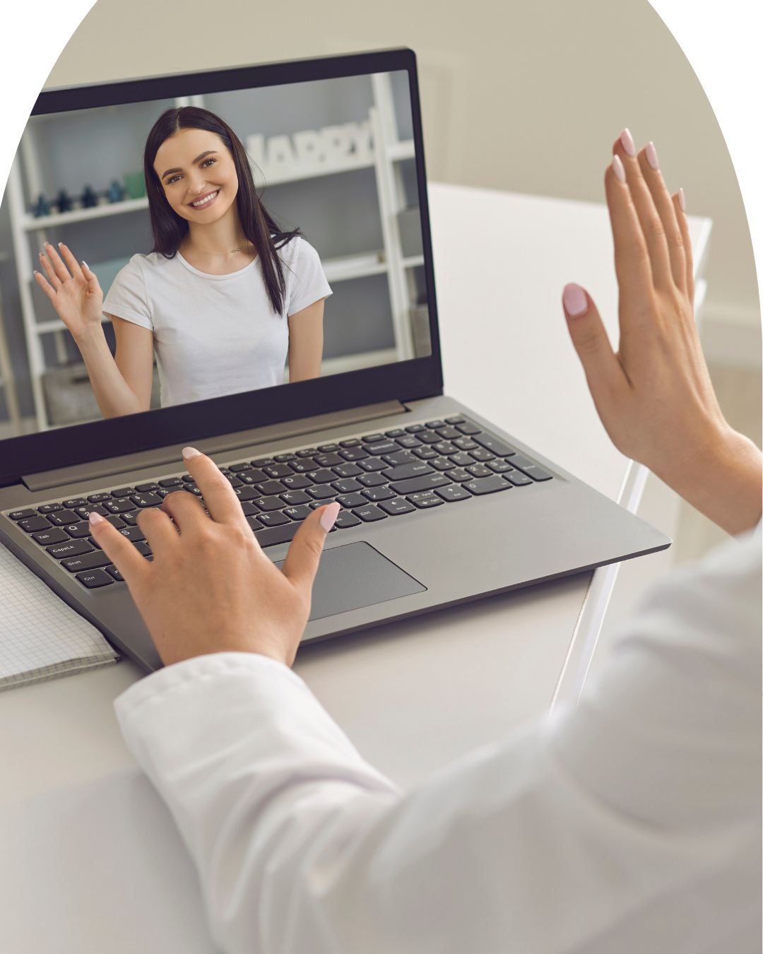 A person on a video call, waving at a woman on the computer screen who is smiling and waving back.