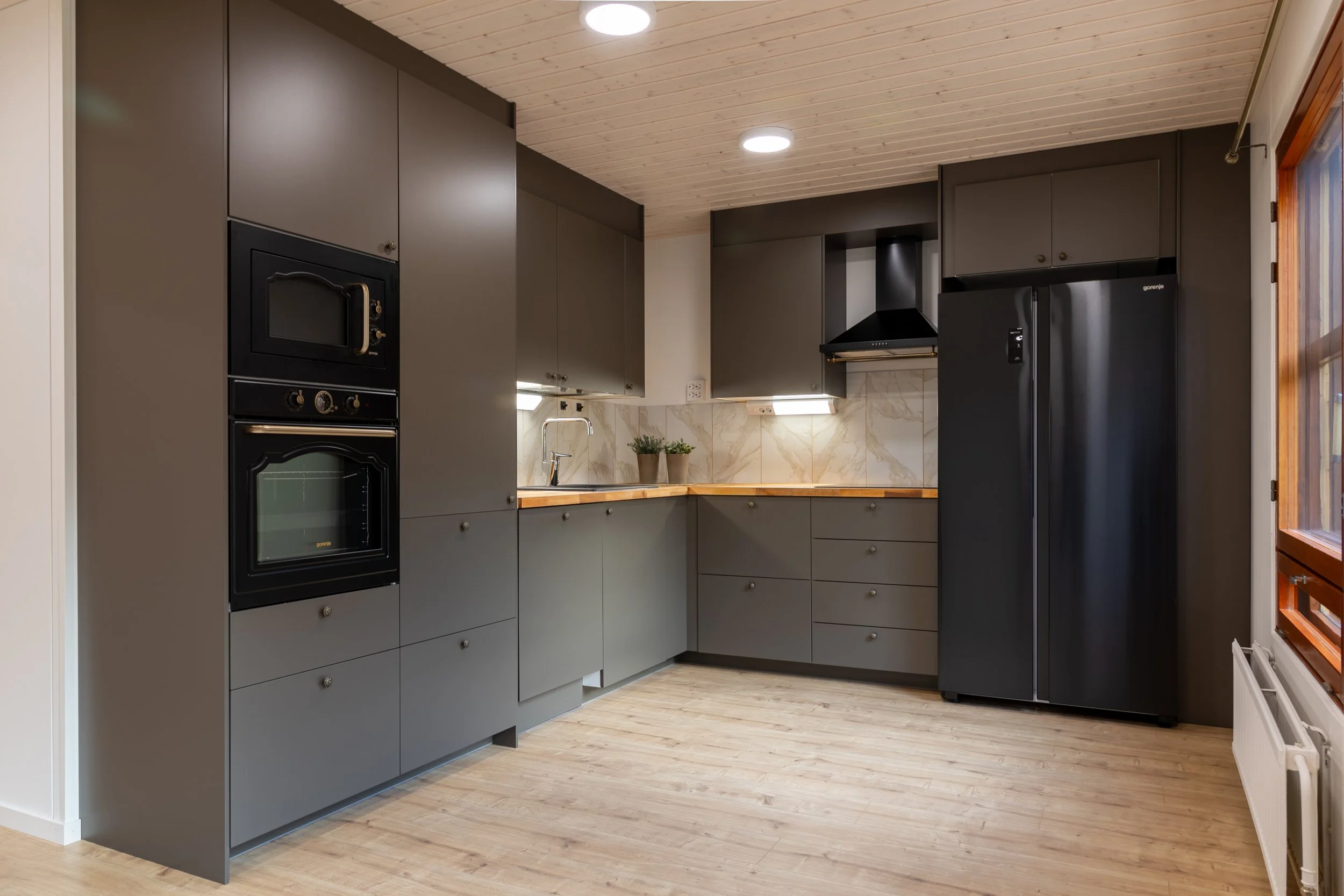 Modern kitchen with gray cabinets, black appliances, a wooden countertop, and a window with wooden trim.