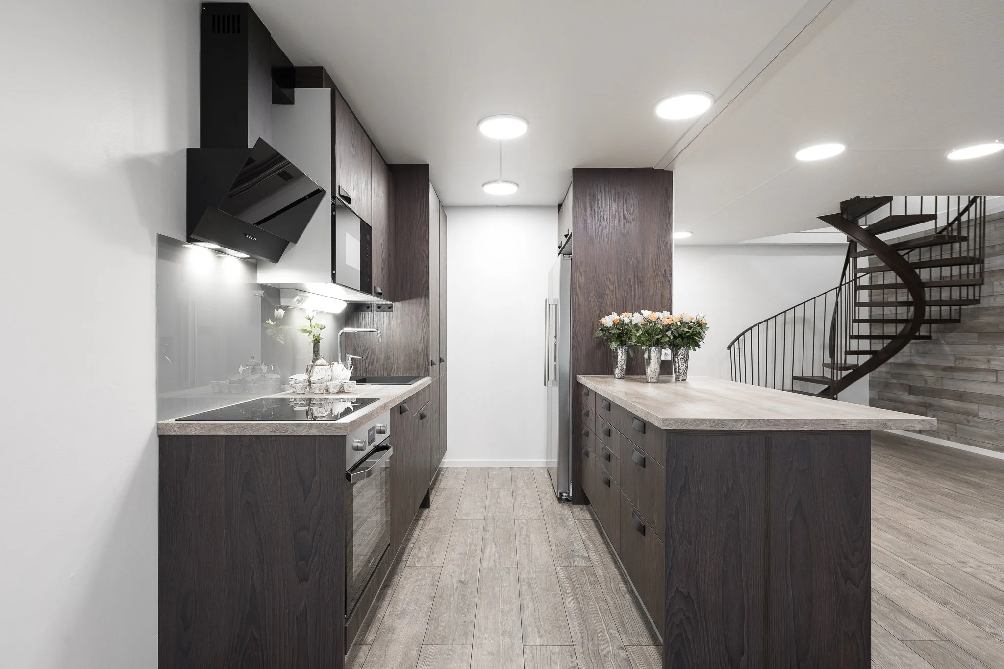 Modern kitchen with dark wood cabinetry, a pendant light, a kitchen island with flowers, a spiral staircase, and wood flooring.