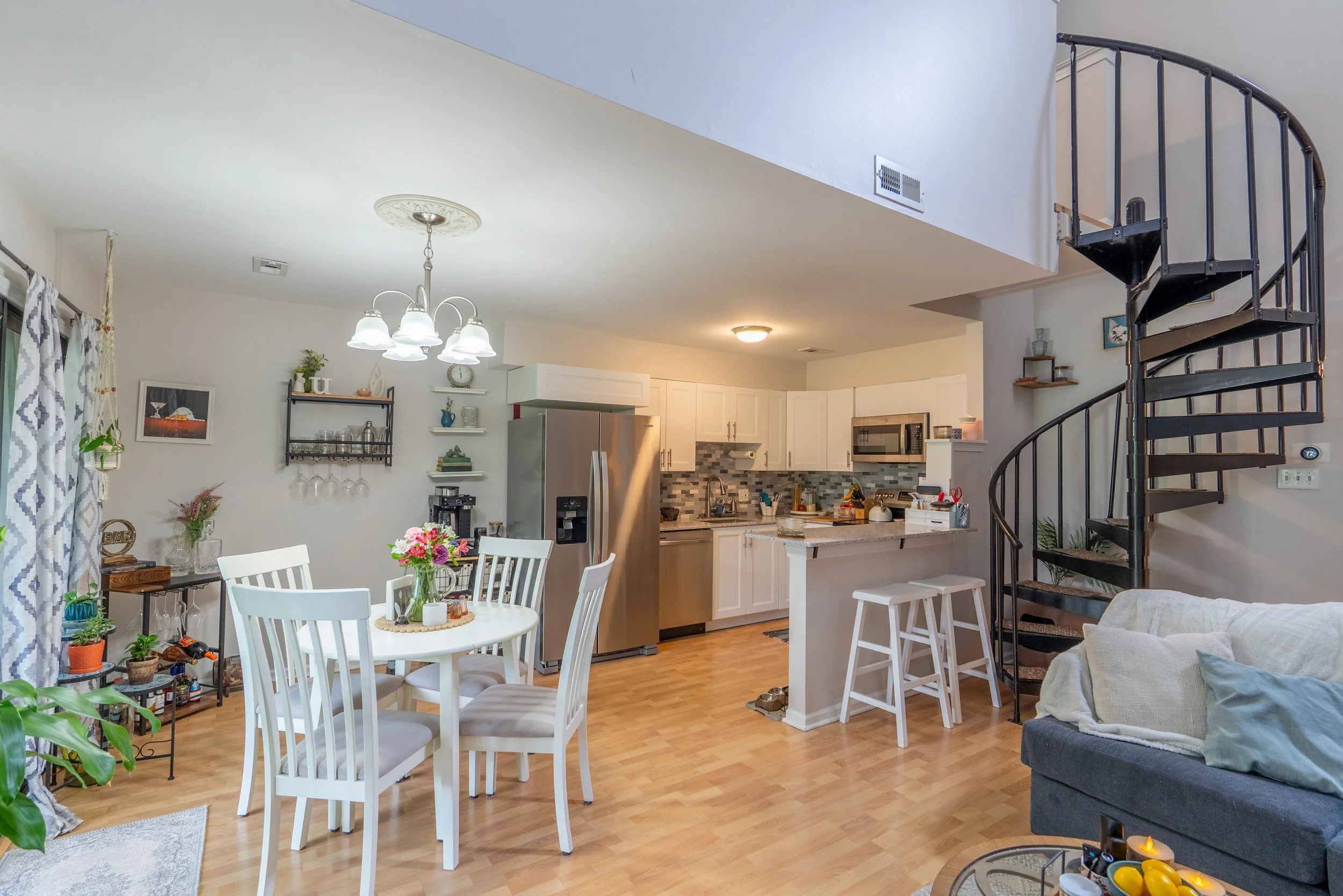 Living room and kitchen area with a dining table, couch, spiral staircase, and kitchen appliances.