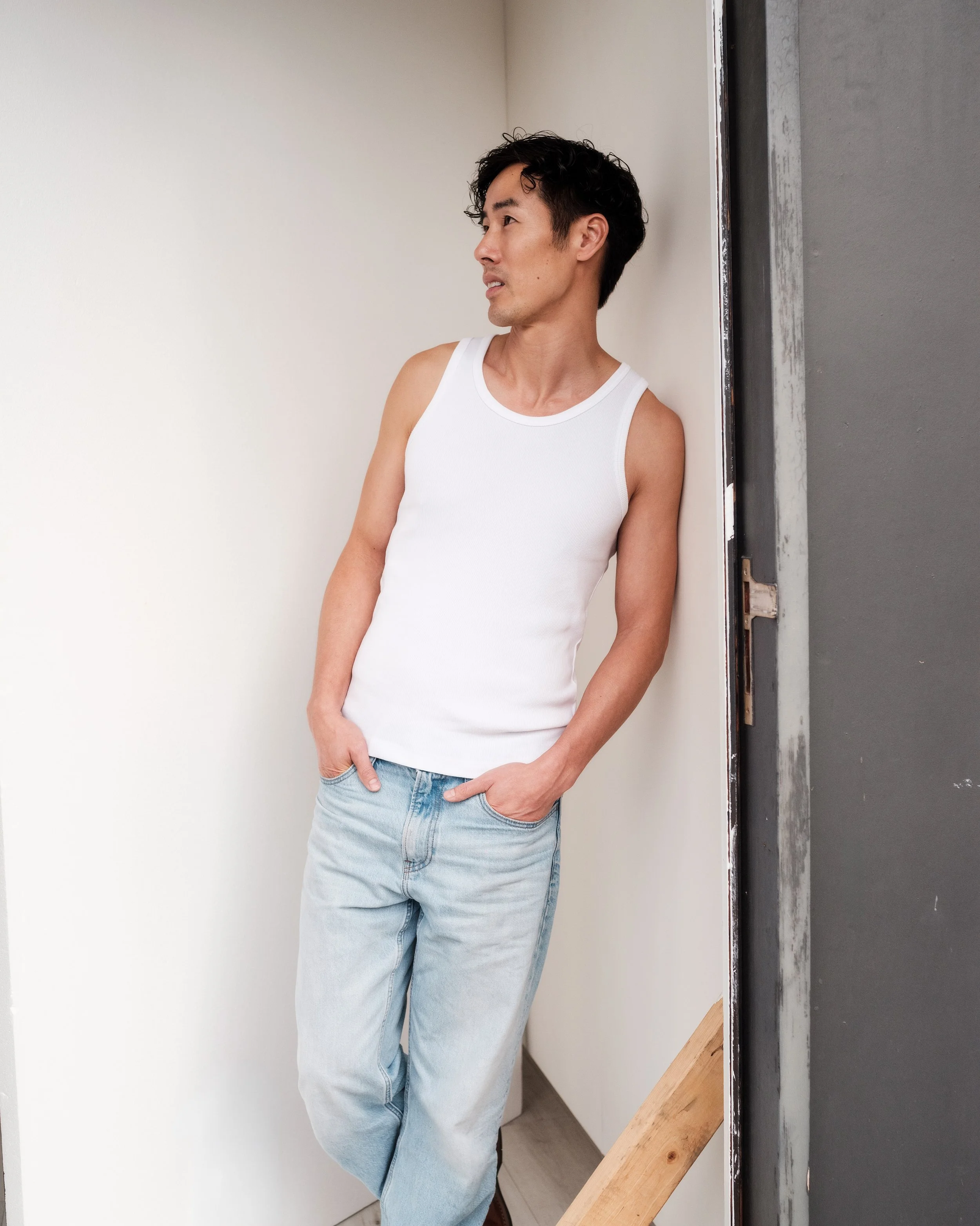 Ray Yee in a white singlet and jeans, standing side on, model digitals