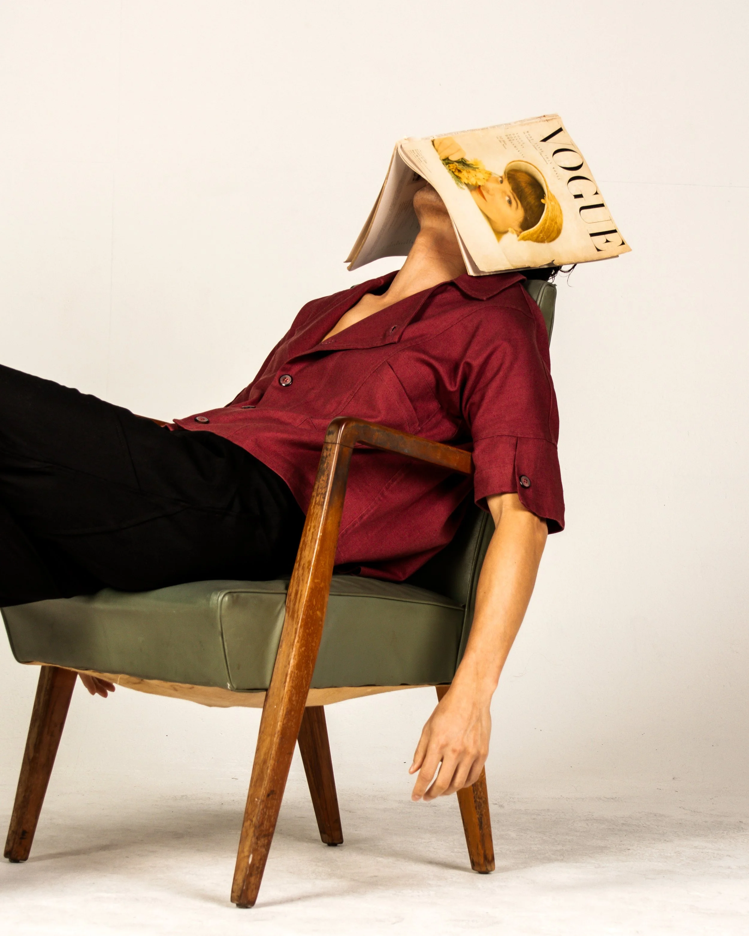 Person sitting in a chair with a magazine covering their face.