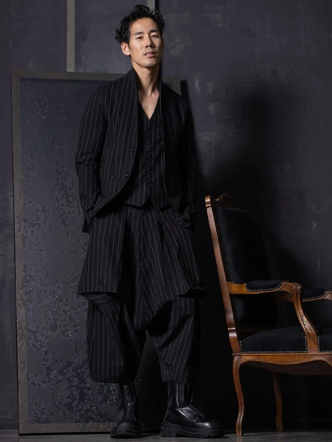 Ray Yee in a black pinstripe suit and waistcoat beside a wooden chair