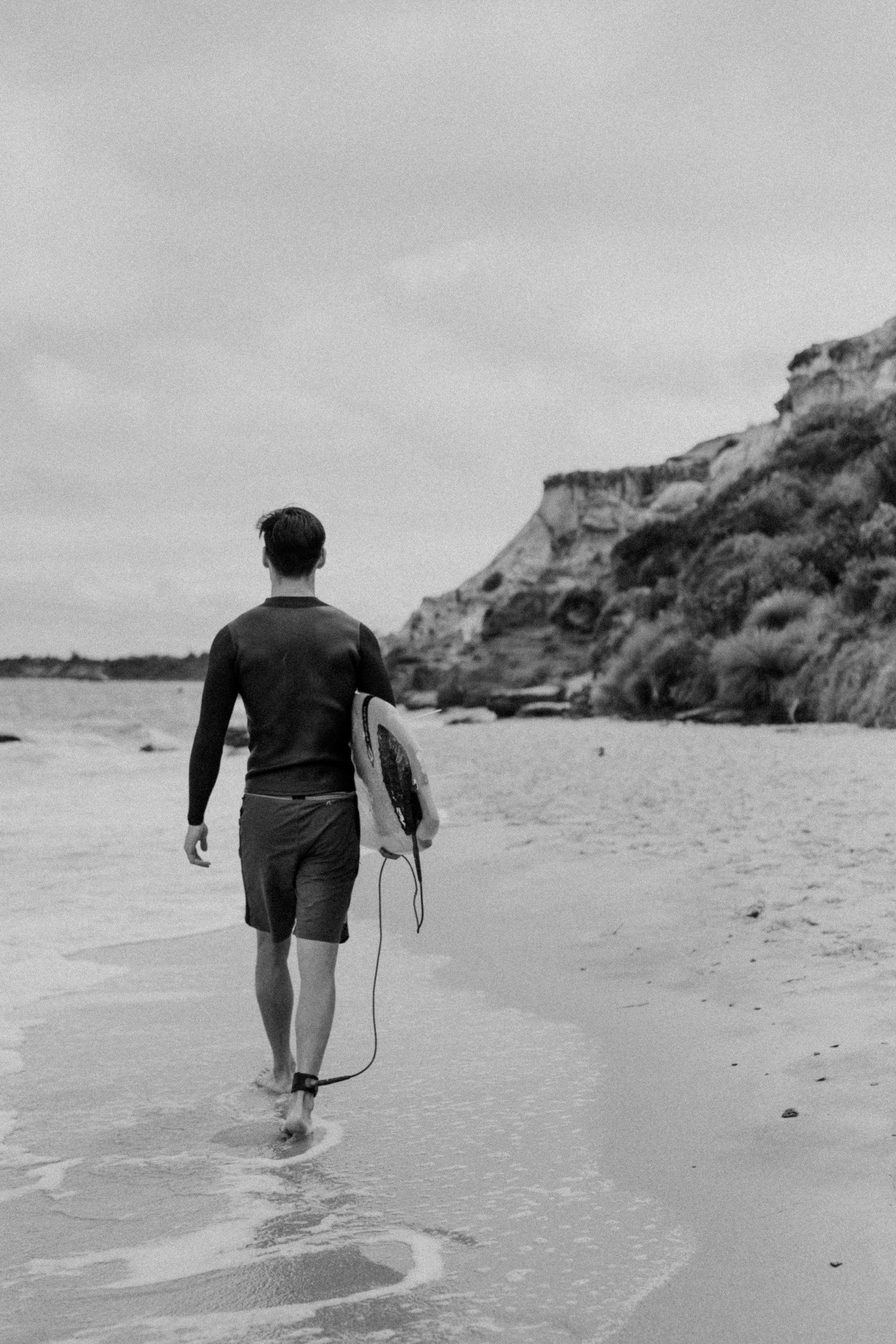 Ray Yee, Asian male model in Melbourne, walking on a beach carrying a surfboard