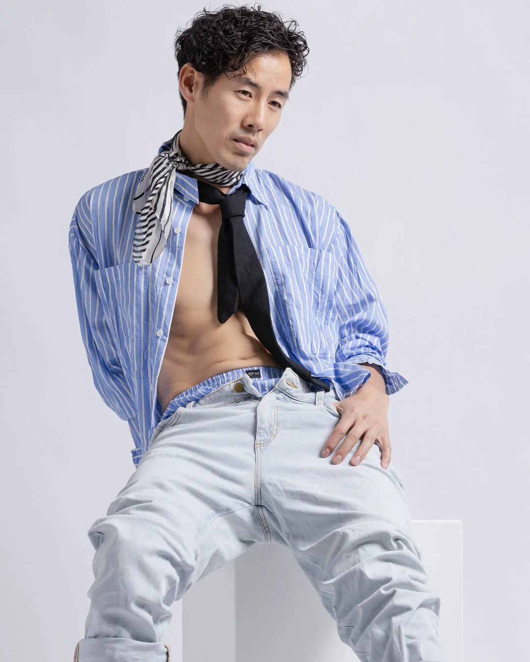 Ray Yee in an open blue striped shirt, black tie and pale jeans
