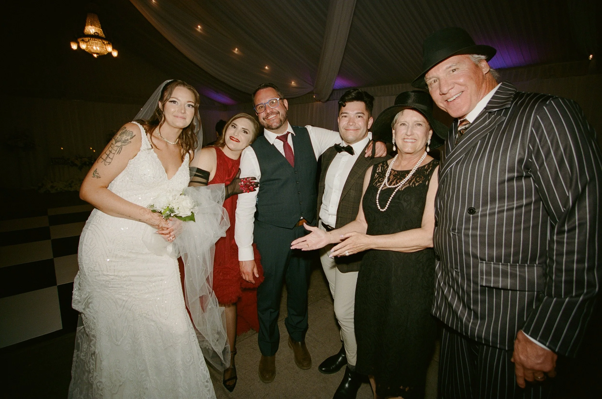 Group of seven people at a wedding reception, smiling and standing together, with the bride holding a bouquet.