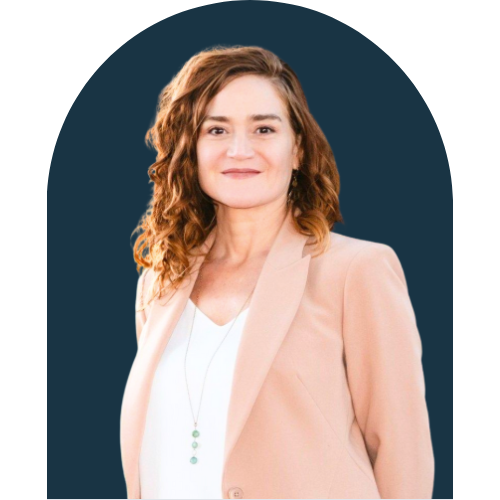 Portrait of a woman with shoulder-length curly hair wearing a beige blazer and white top, smiling against a dark blue background.