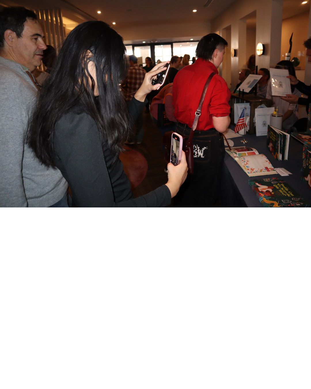 People at a booth with books and small American flags in a crowded indoor space, possibly at a book fair or event.