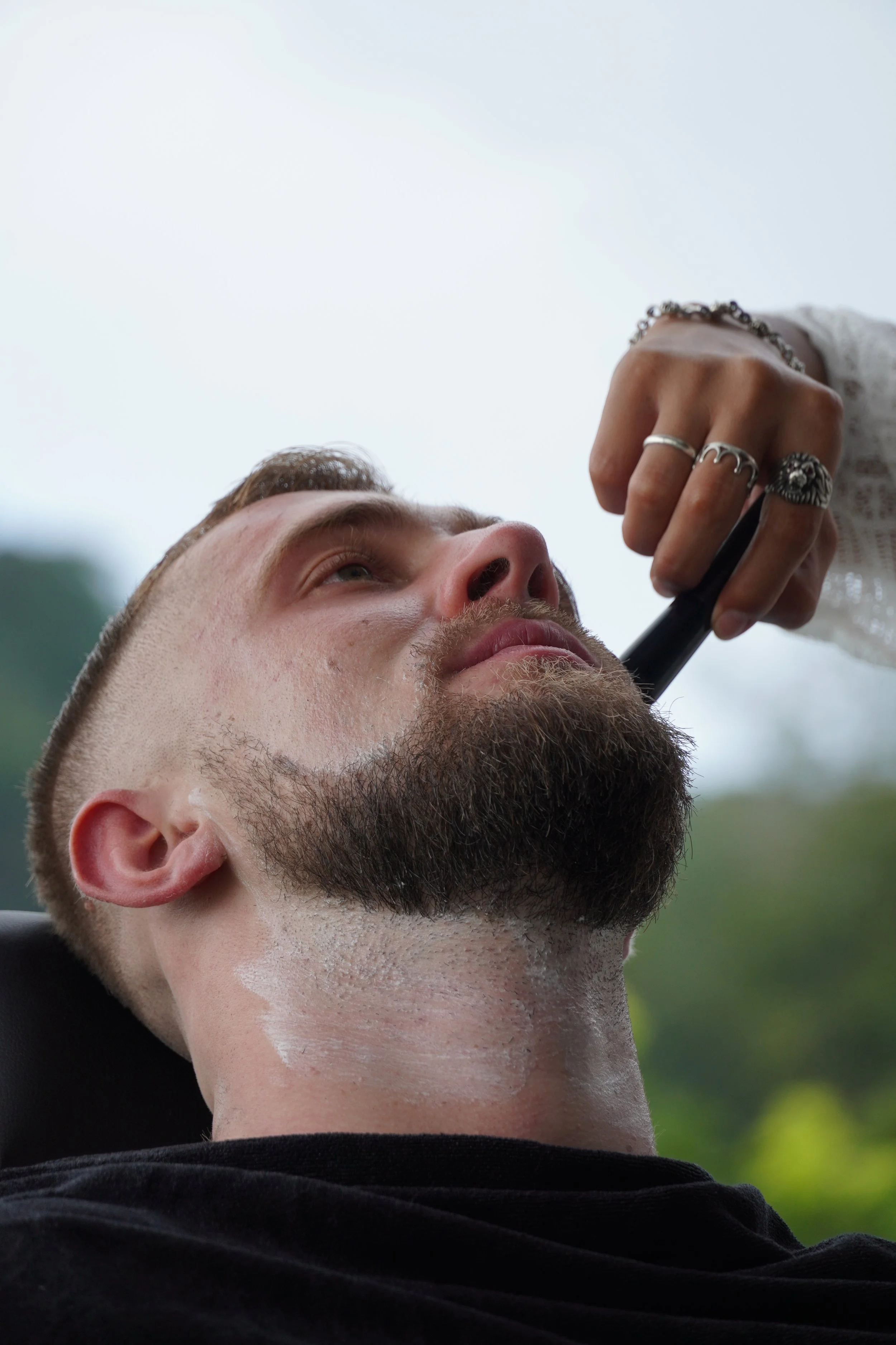 Man receiving a shave outdoors with a straight razor.