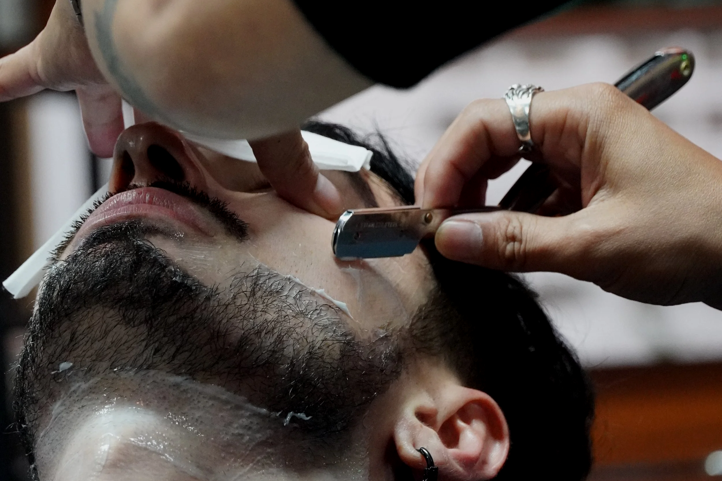 A person getting a straight razor shave, with a barber applying shaving cream to the person's face.