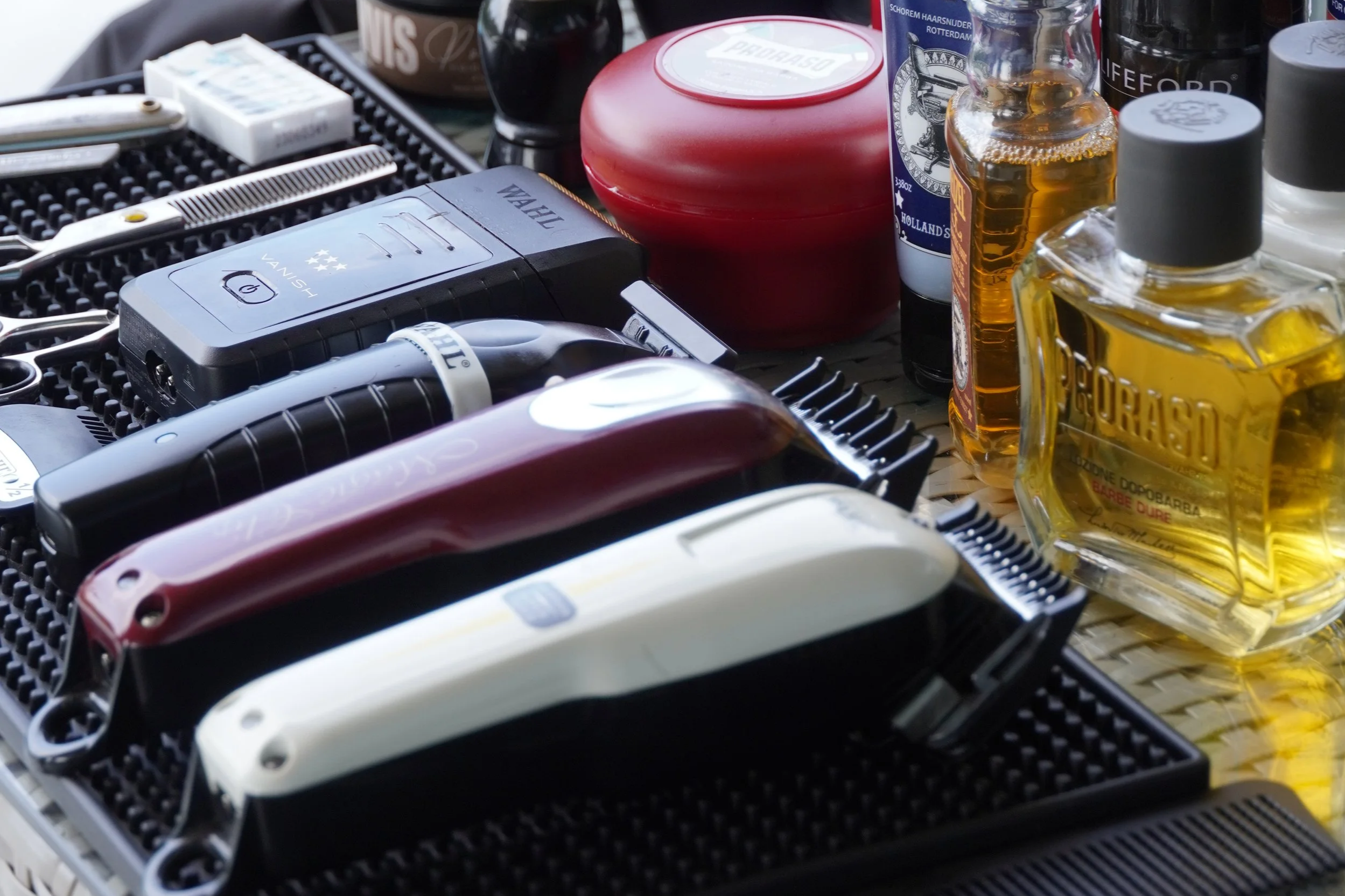 Collection of hair grooming products including clippers, trimmers, and bottles of hair oil, alcohol, and grooming accessories on a textured surface.