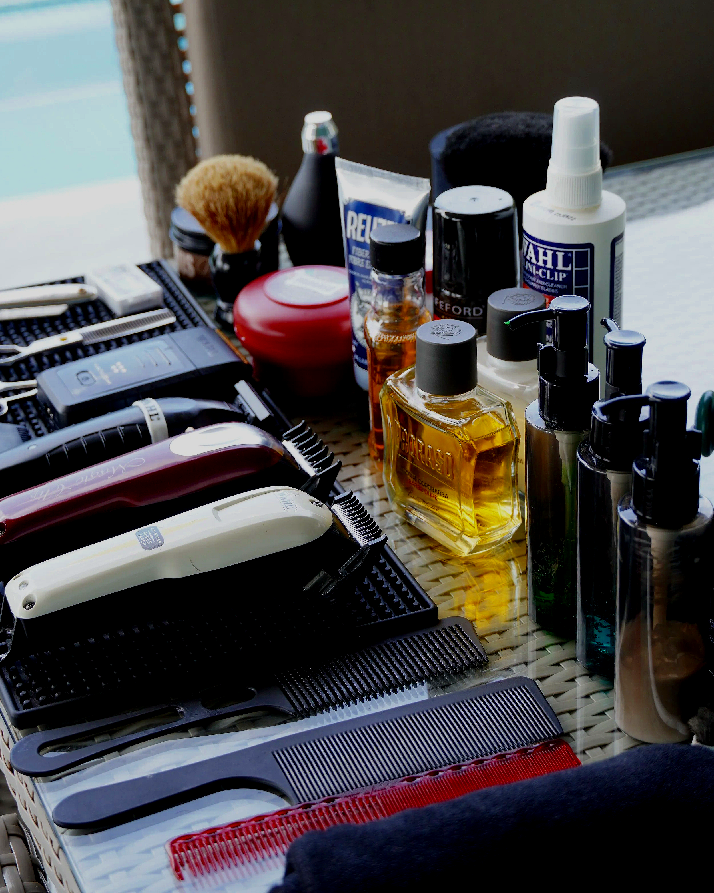 Collection of hair grooming tools, including clippers, scissors, combs, and various bottles of hair products on a table.