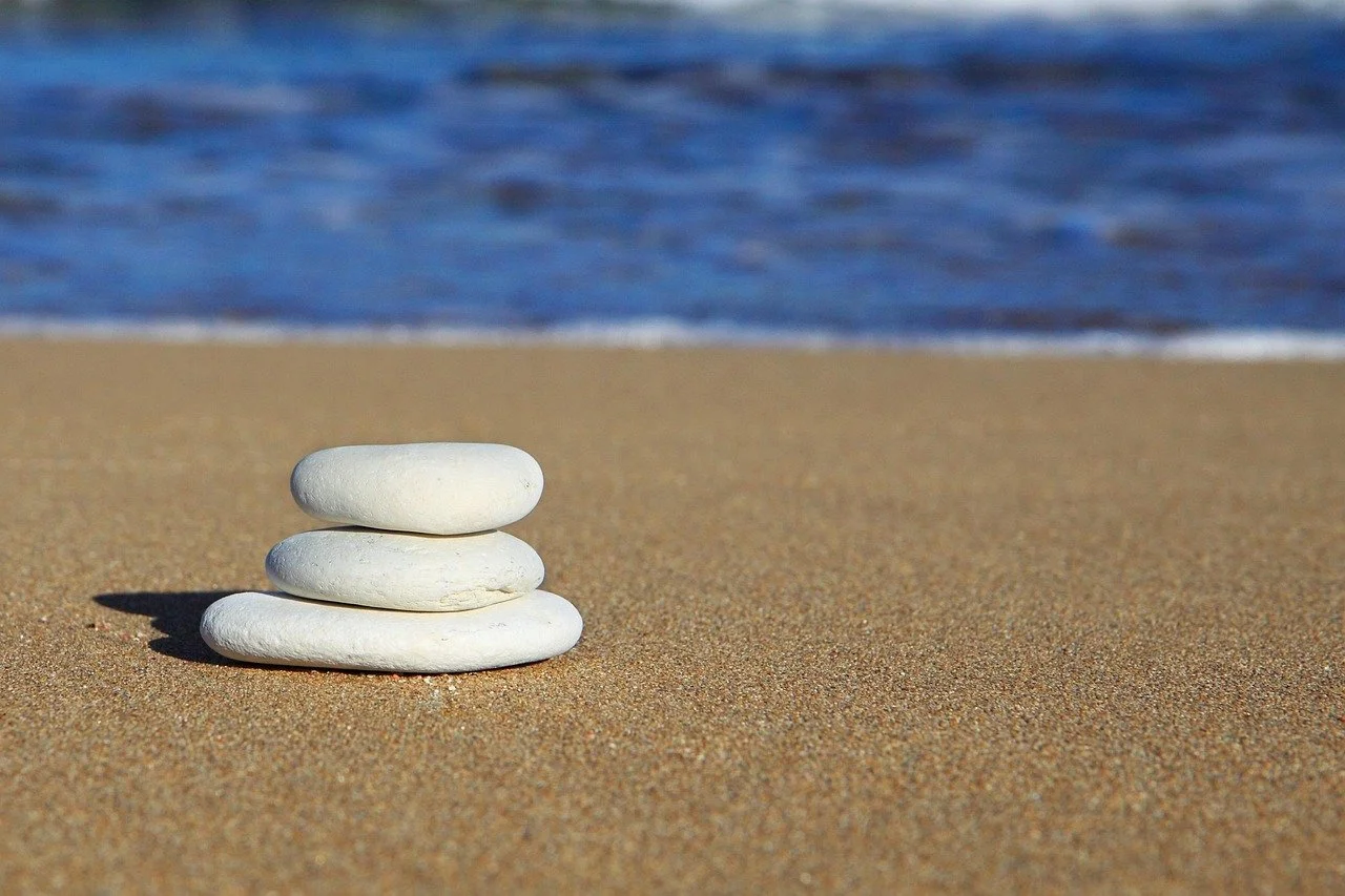 Stacked white rocks on a sandy beach with the ocean in the background.