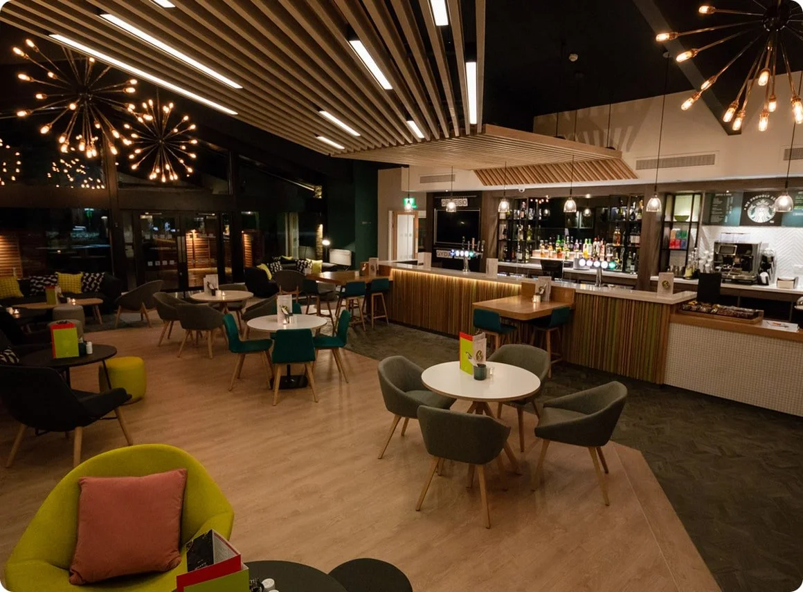 Interior of a modern bar and lounge with wooden ceiling beams, stylish lighting fixtures, and a well-stocked bar area.