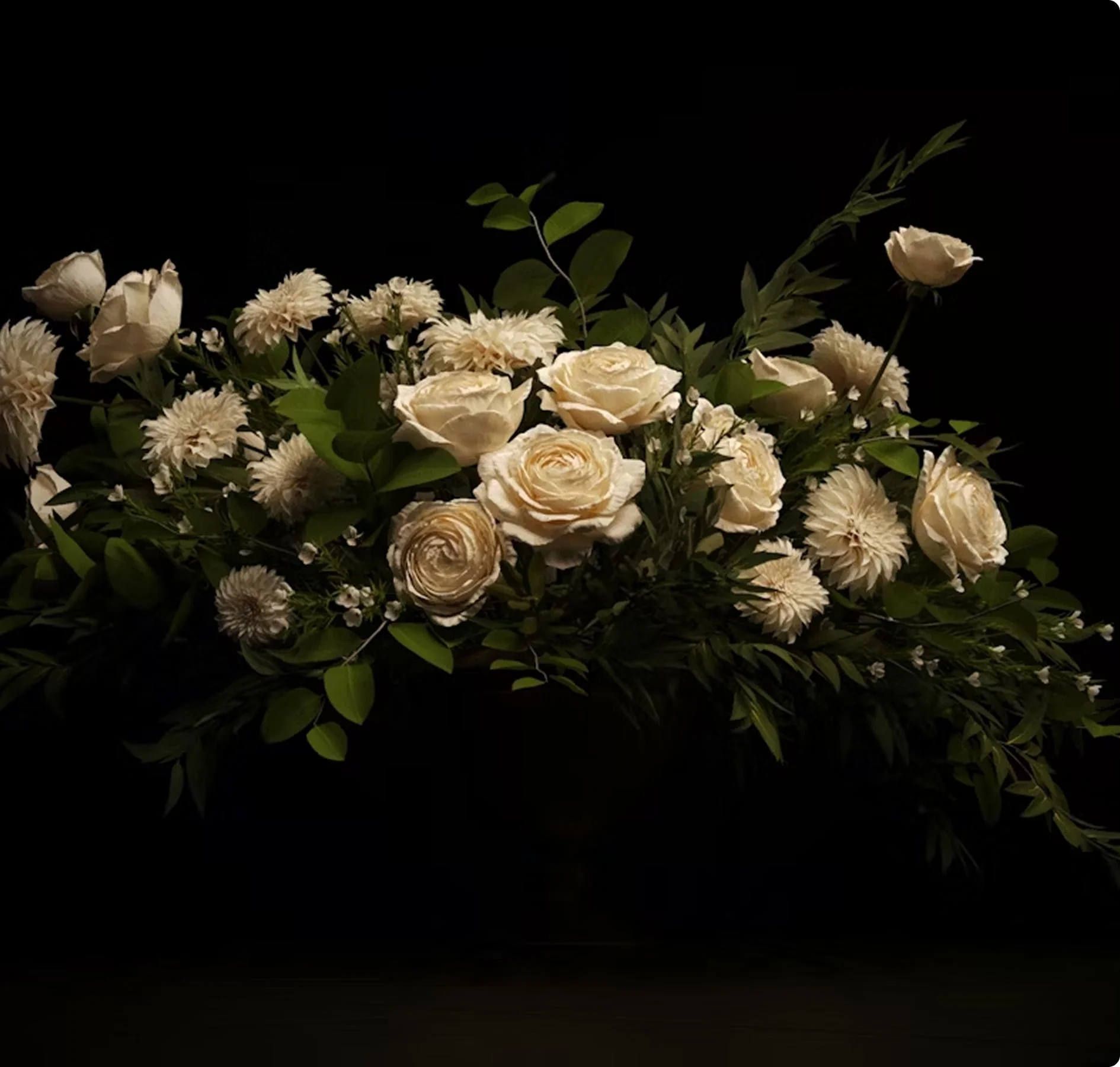 Arrangement of white and cream flowers with green leaves against a black background.