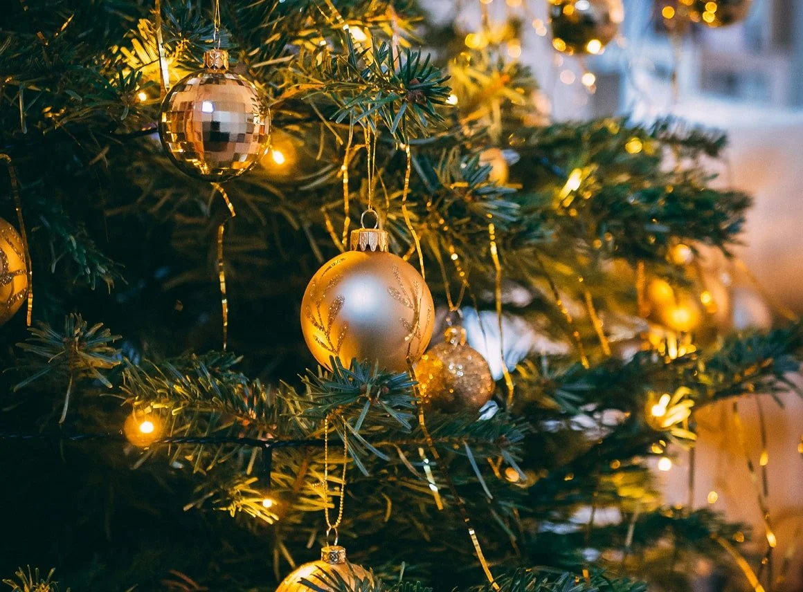 Close-up of a decorated Christmas tree with gold and silver ornaments and yellow lights.