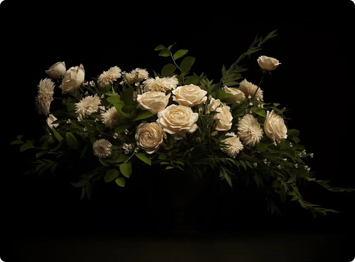 White roses and other white flowers with green leaves against a black background.