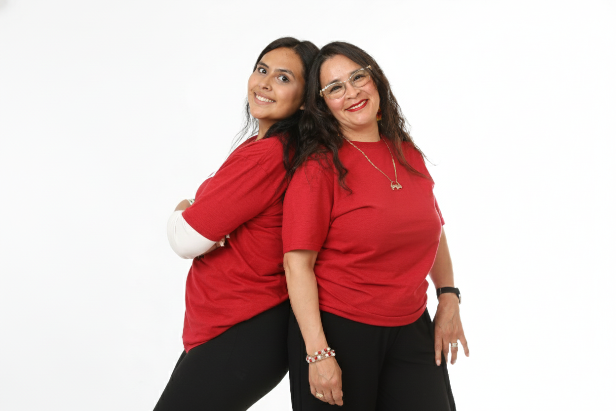 Two women, one younger and one older, smiling back-to-back while standing against a plain white background. Both are wearing red tops and black bottoms.