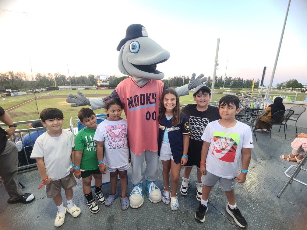 Group of children posing with mascot at baseball stadium during evening game.