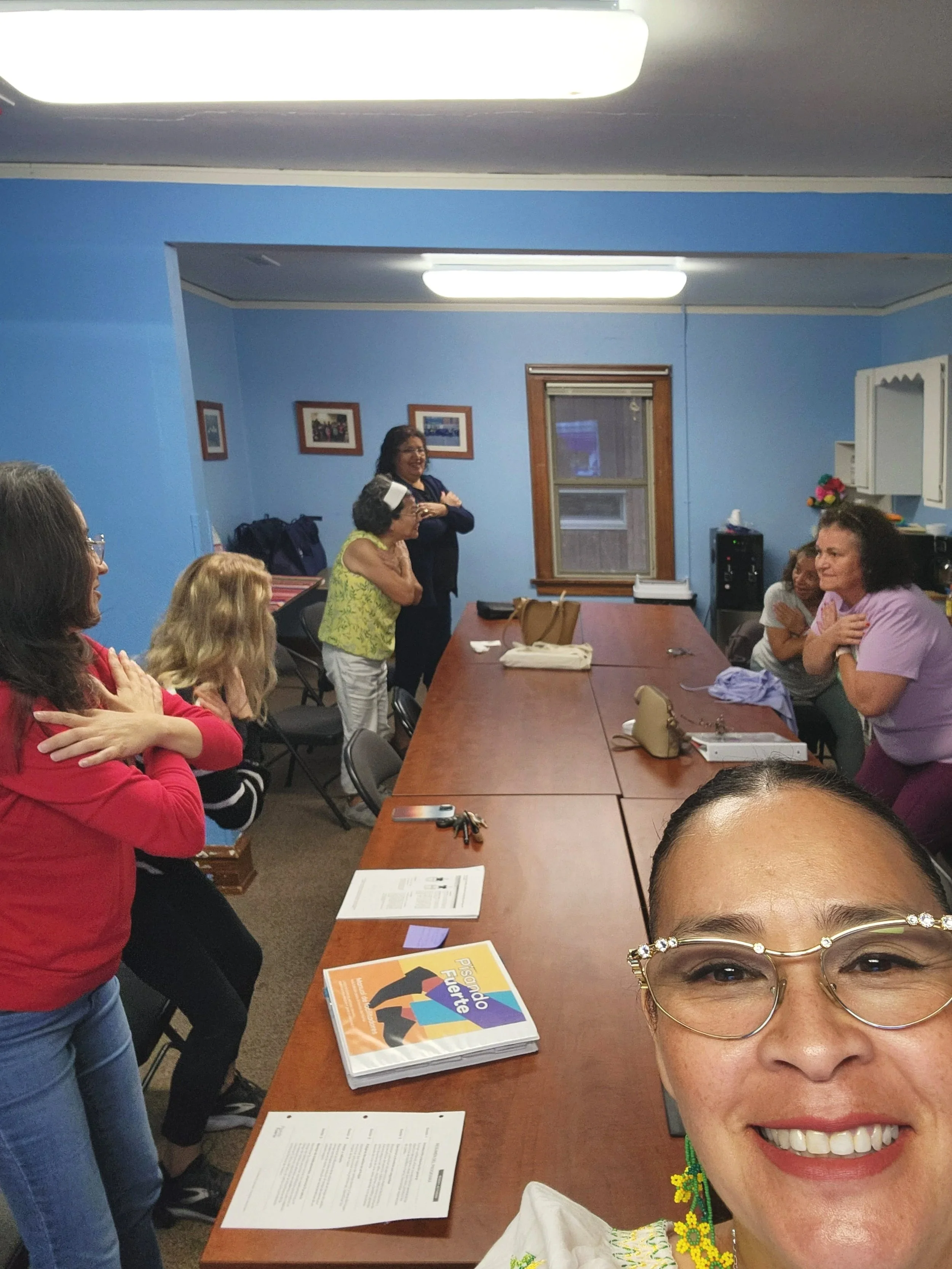 Group of women participating in a heartfelt activity on a conference table in a room with blue walls and framed pictures.