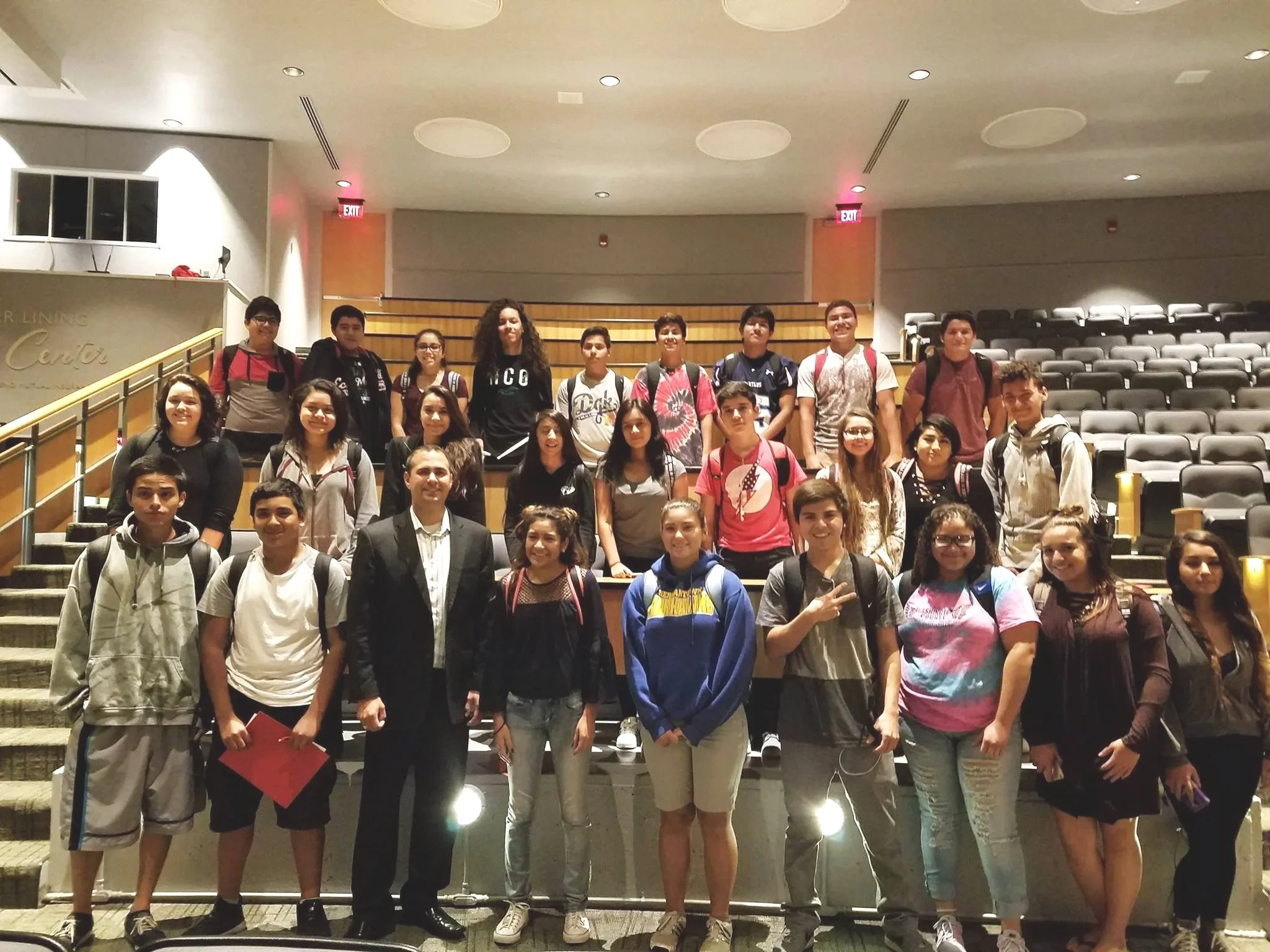Group of students and teachers posing on stairs inside a building, likely a school or auditorium.