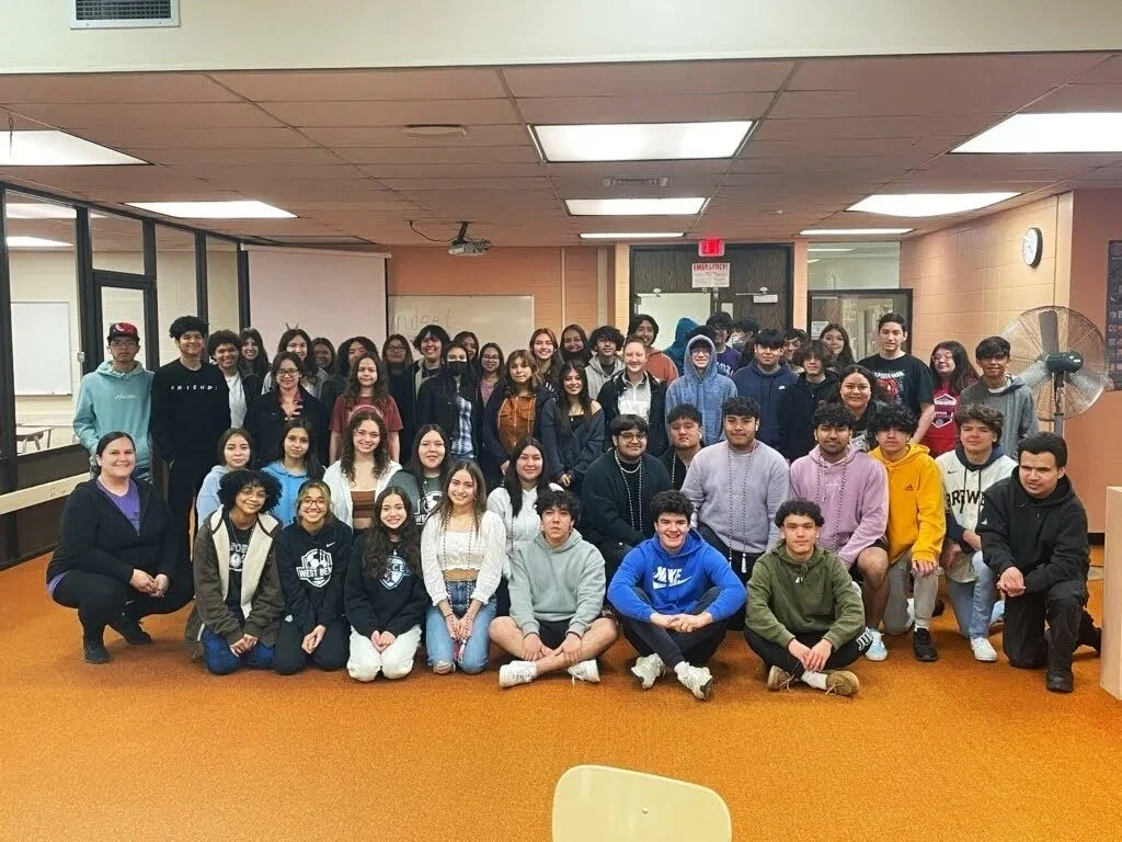 Group photo of diverse students and teachers in a school classroom or community center.
