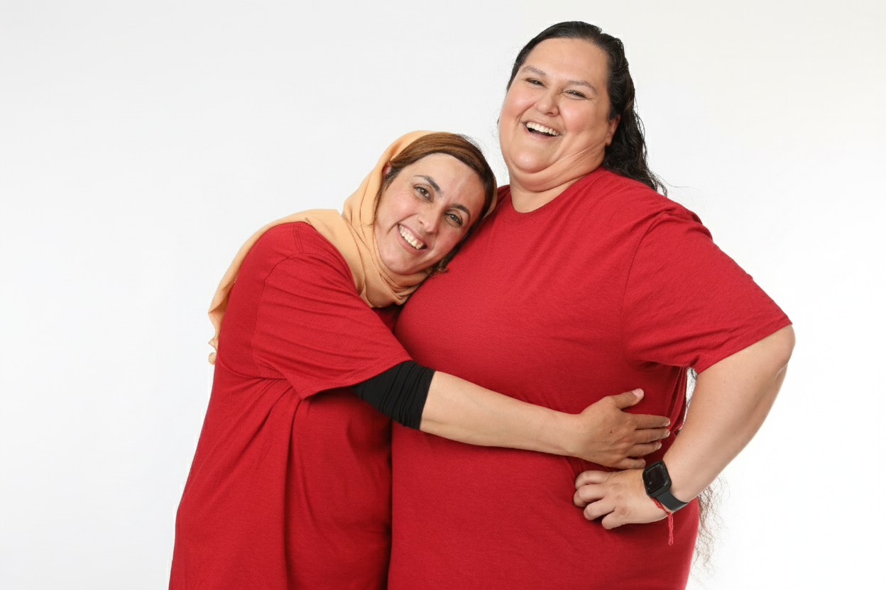 Two women in red shirts happily hugging and smiling at the camera against a plain white background.