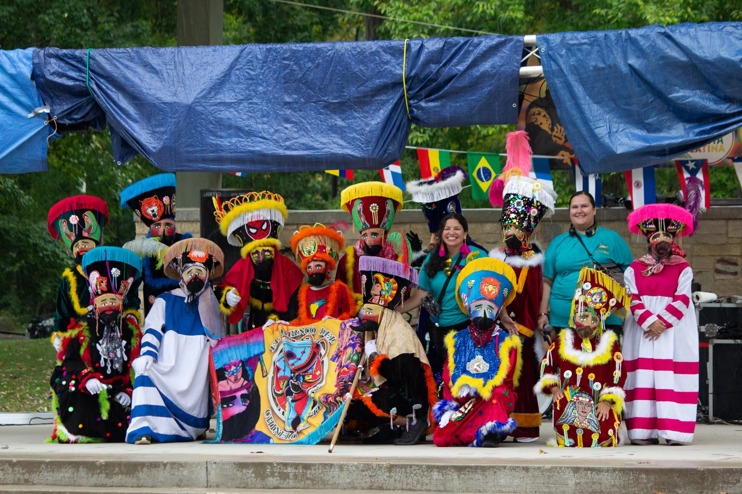 Group of performers dressed in colorful traditional costumes and masks on an outdoor stage for a cultural event.