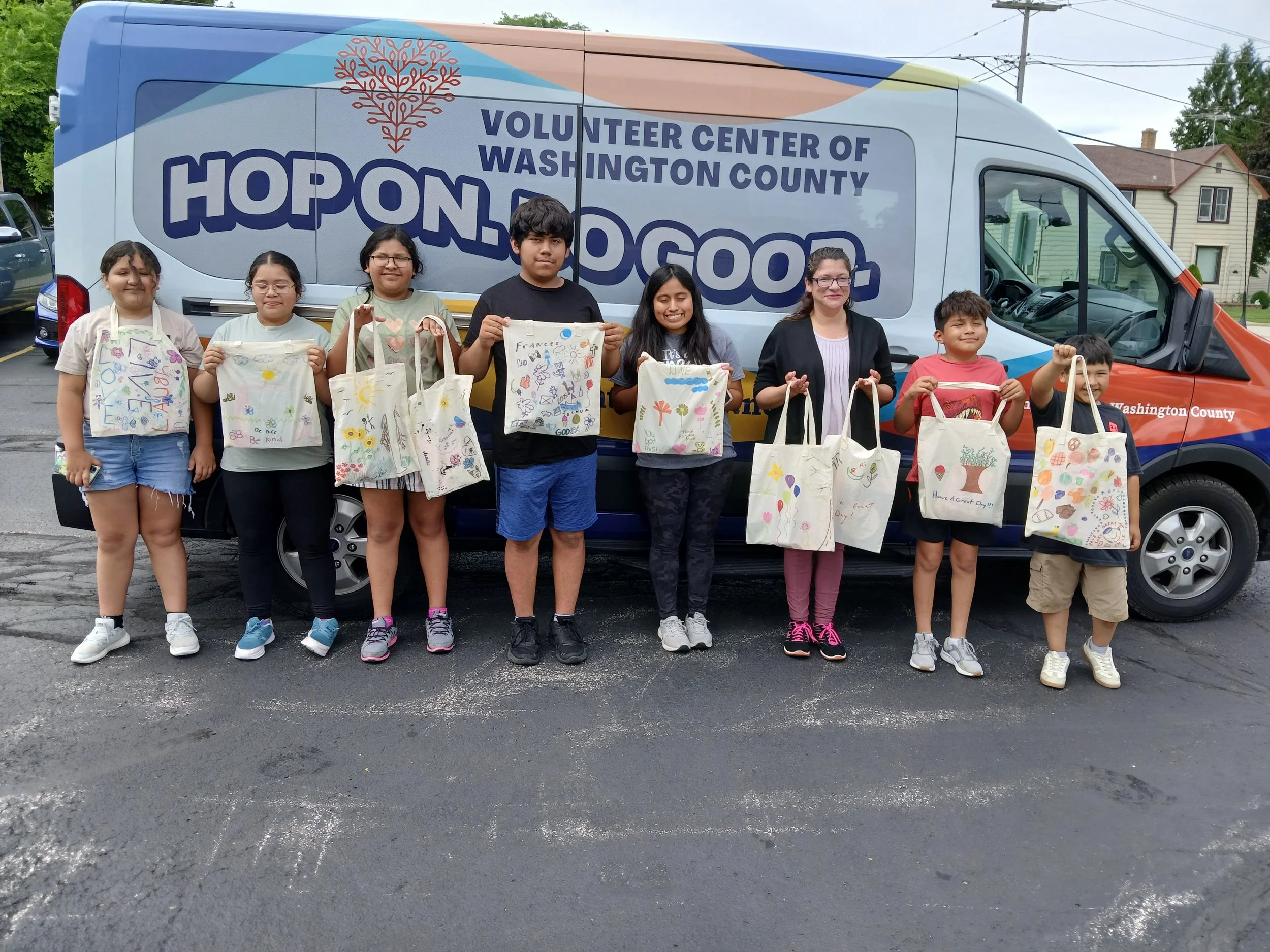 Group of children and an adult holding decorated bags in front of a Washington County volunteer van.