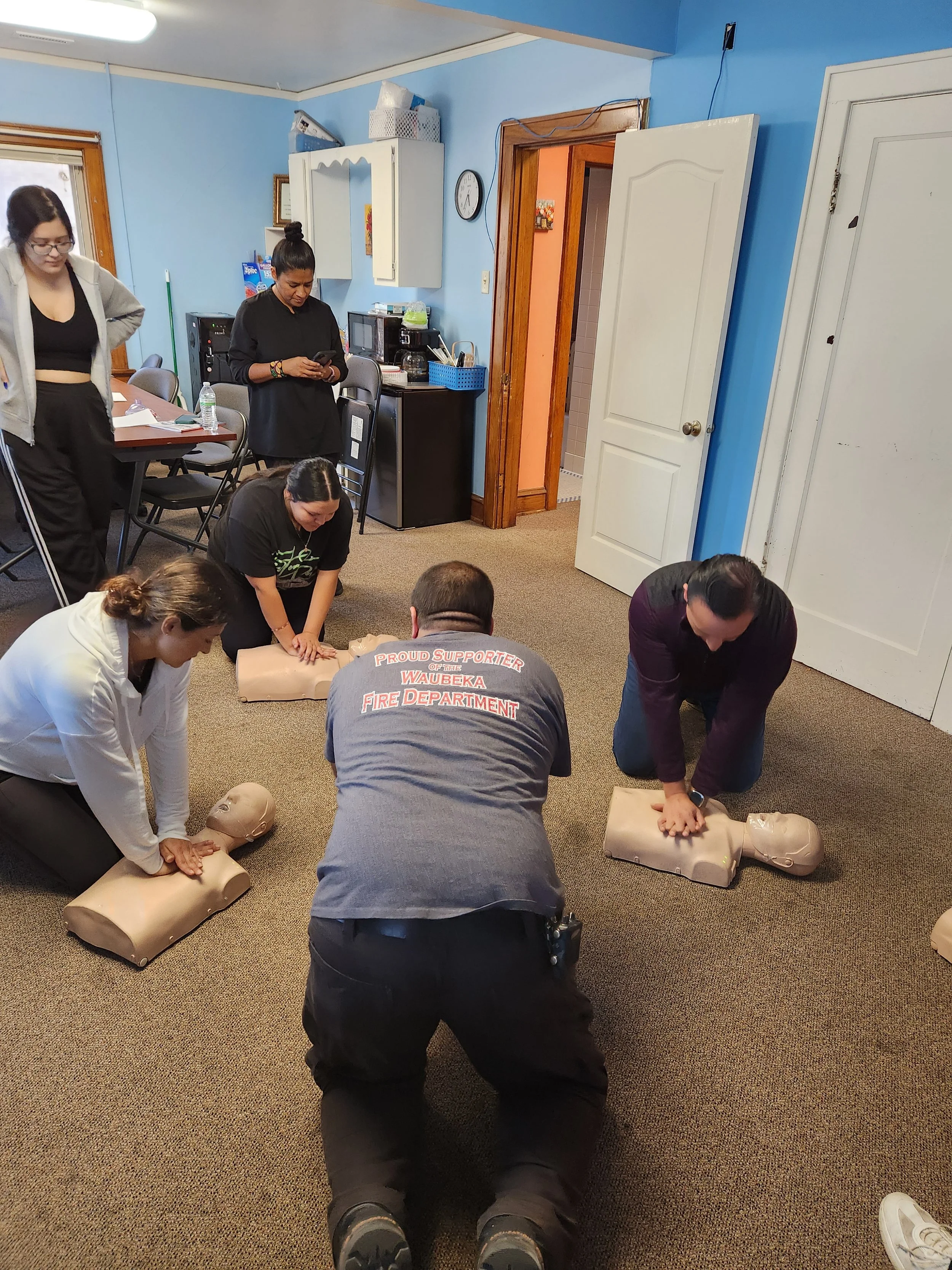 Group of people practicing CPR on mannequins in a classroom setting.