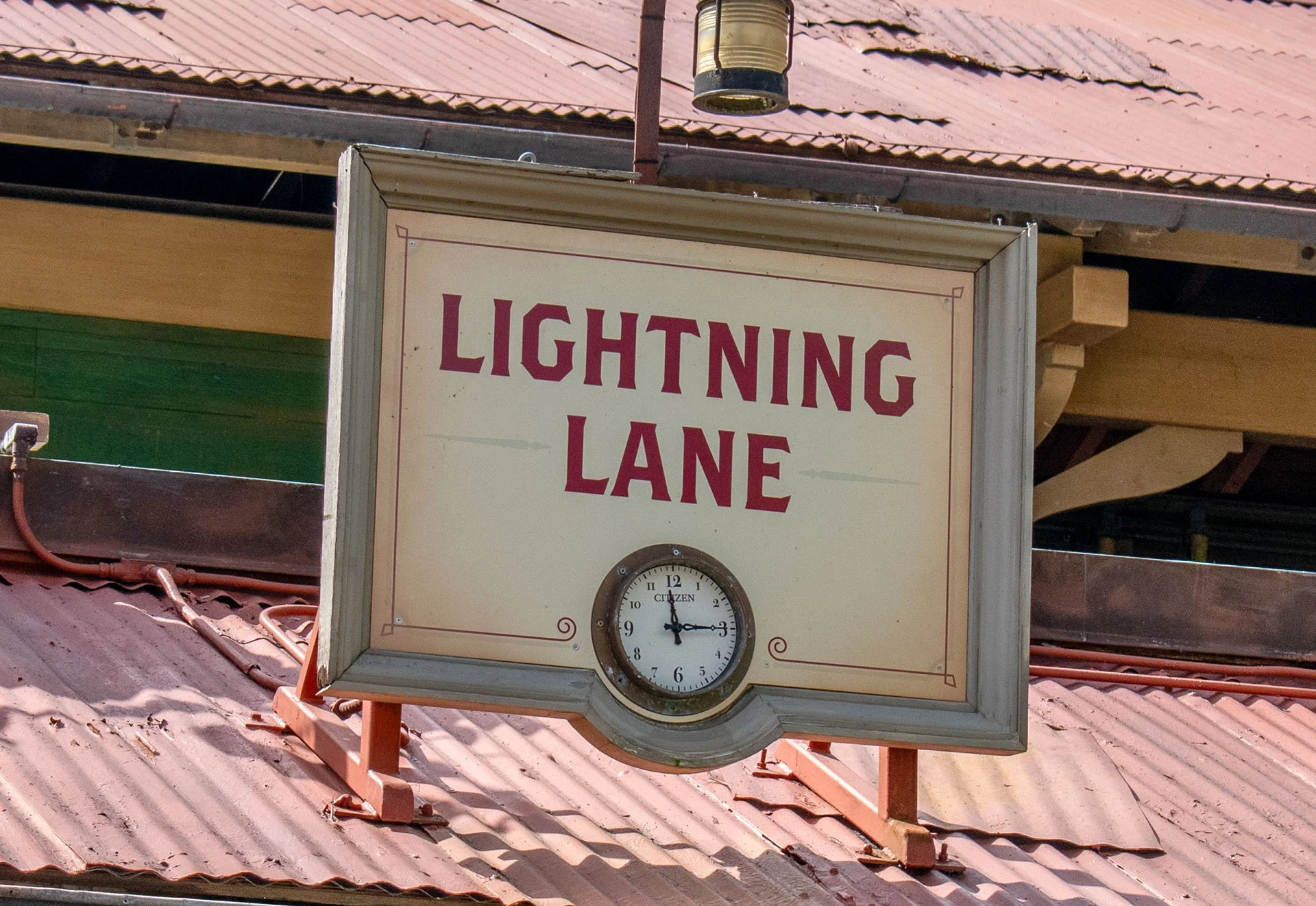 A sign with the words 'Lightning Lane' and a clock showing the time 2:16, mounted on a building with a red metal roof.