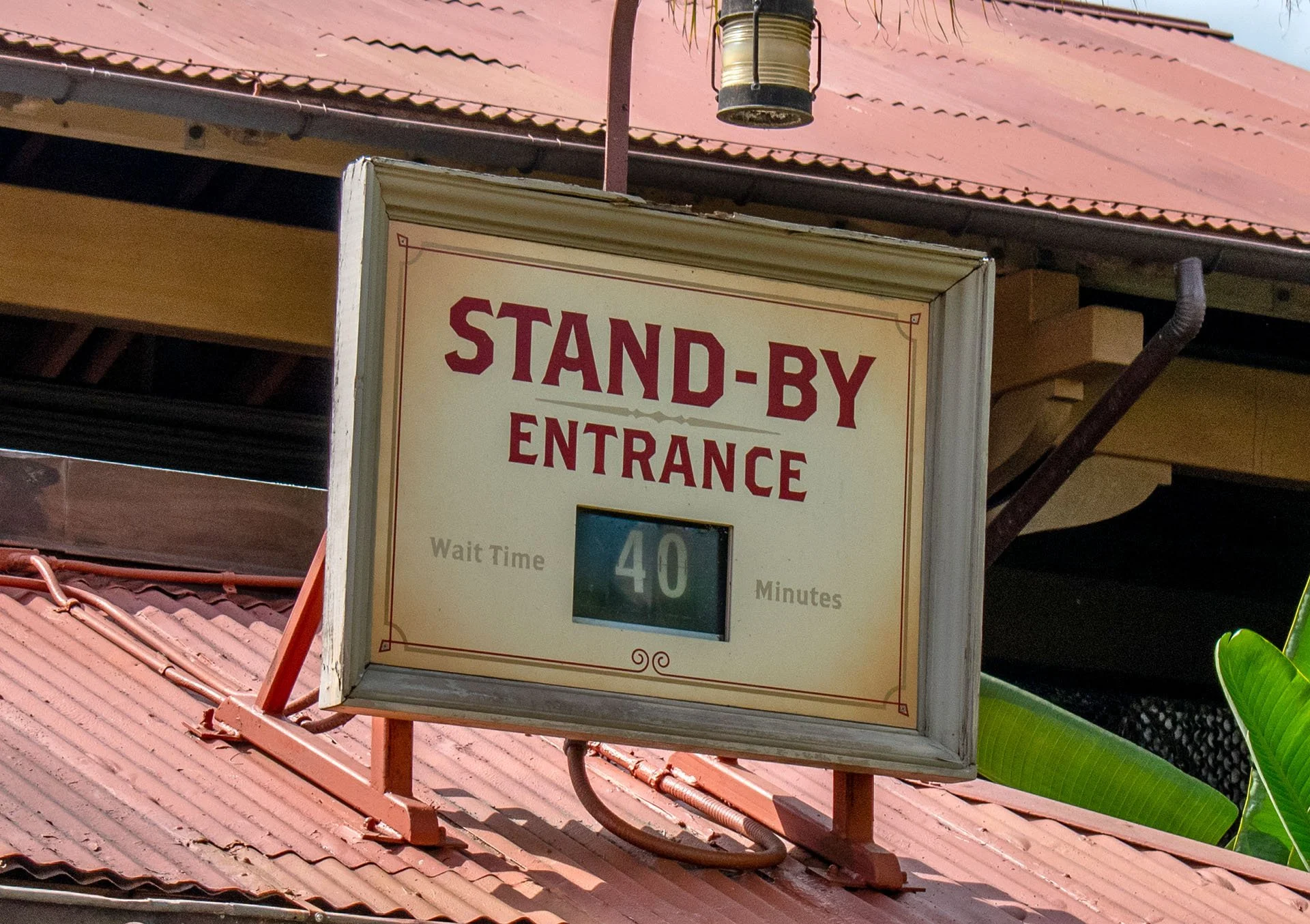 A sign that reads "STAND-BY ENTRANCE" with a digital display showing a wait time of 40 minutes, mounted on a red metal frame on a roof with red tiles.