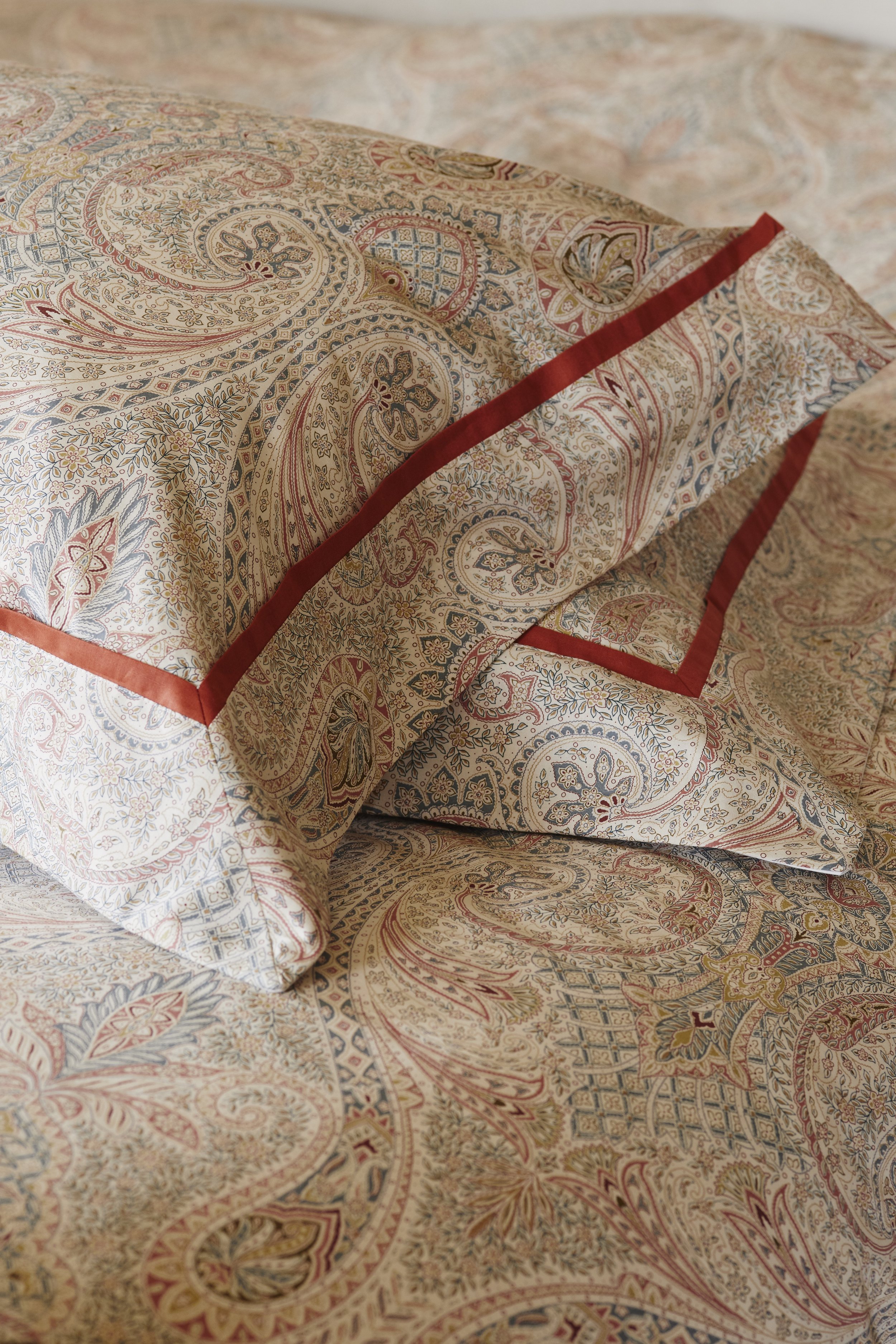 Close-up of a bed with paisley-patterned bedding and matching pillows, featuring intricate designs in beige, red, and blue.