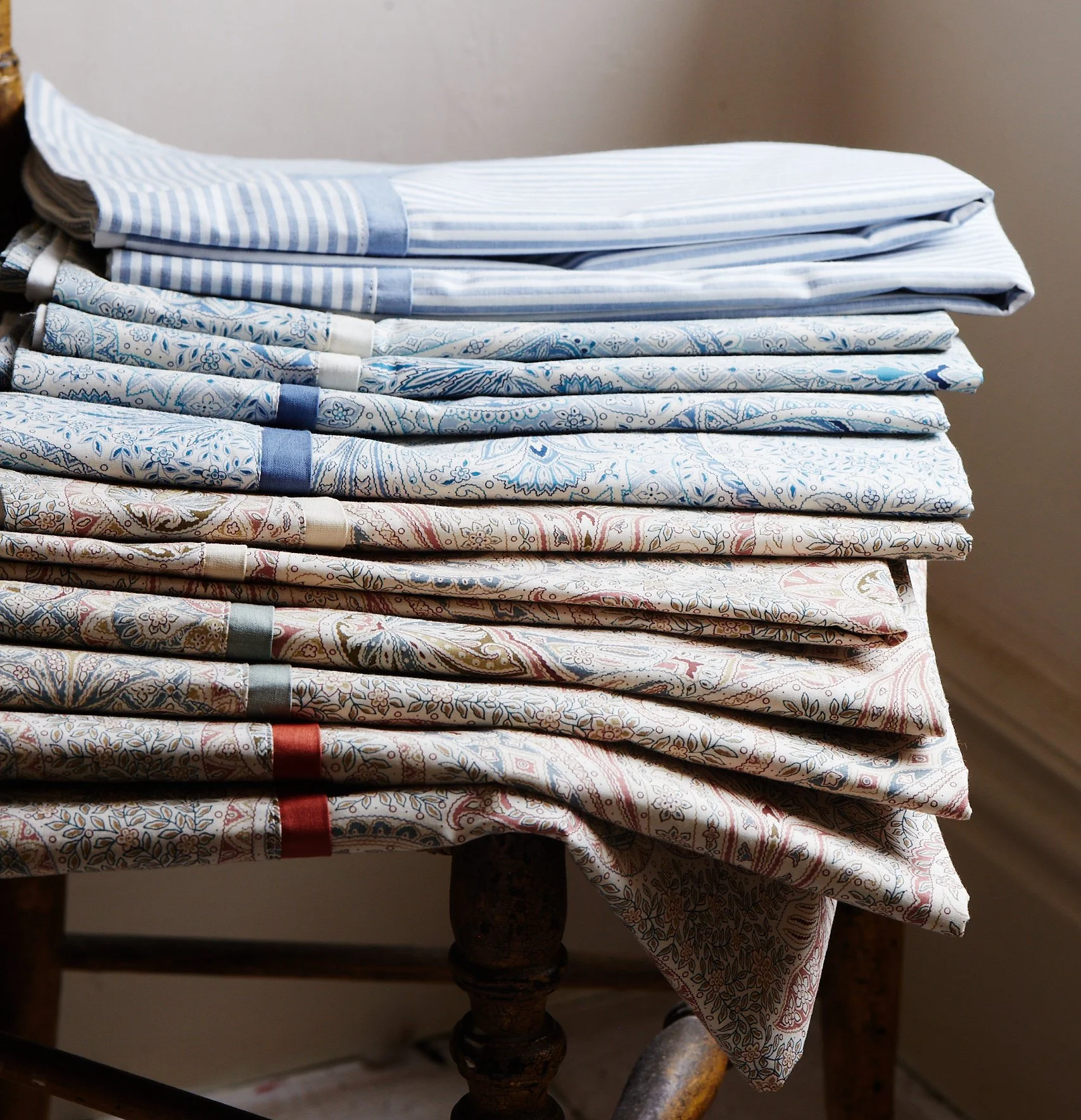 Stack of folded bed sheets and pillowcases with various patterns and colors on a wooden table.