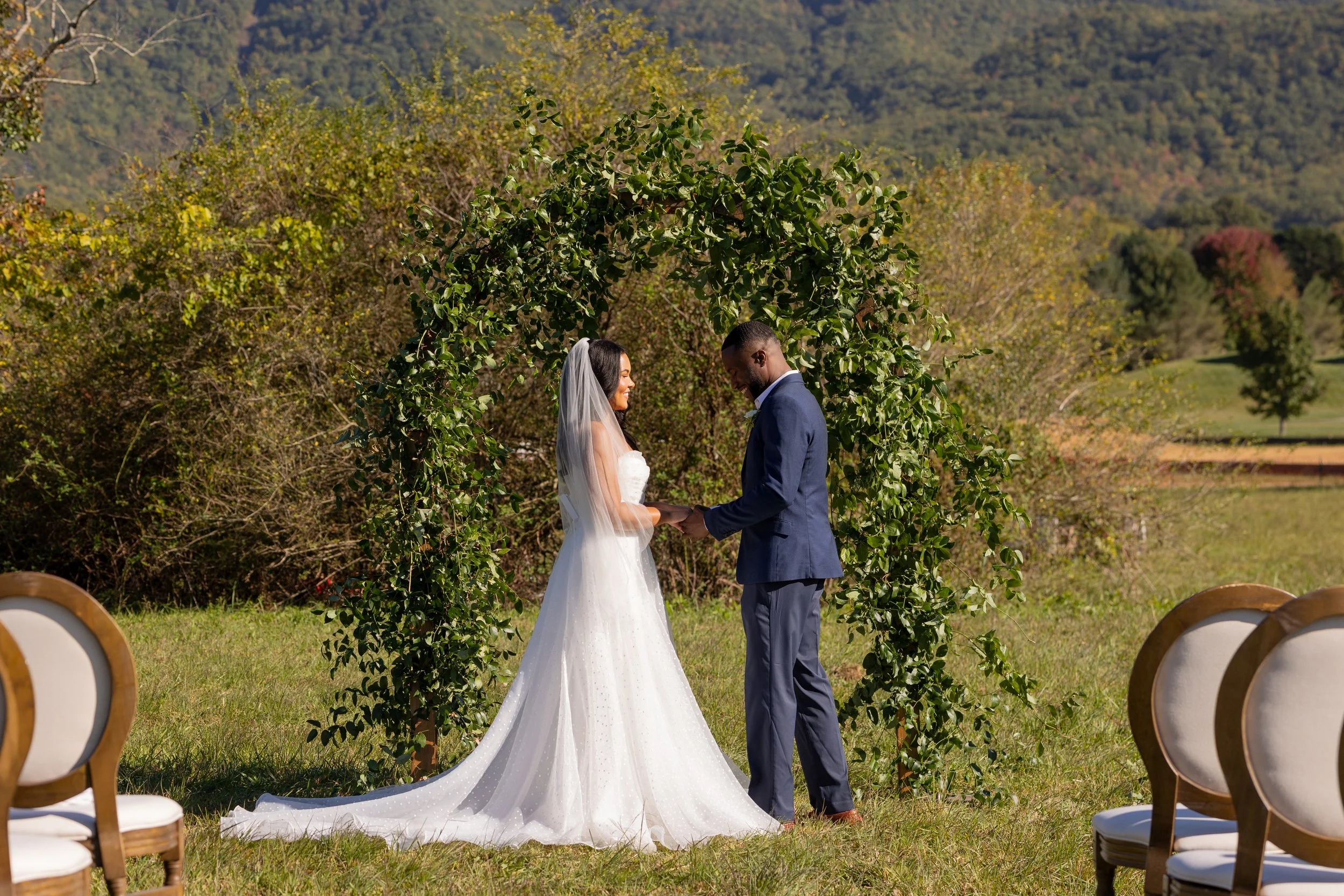 ride and groom holding hands beneath a greenery-covered ceremony arch with Smoky Mountain views at The Lumigail near Gatlinburg, Tennessee.