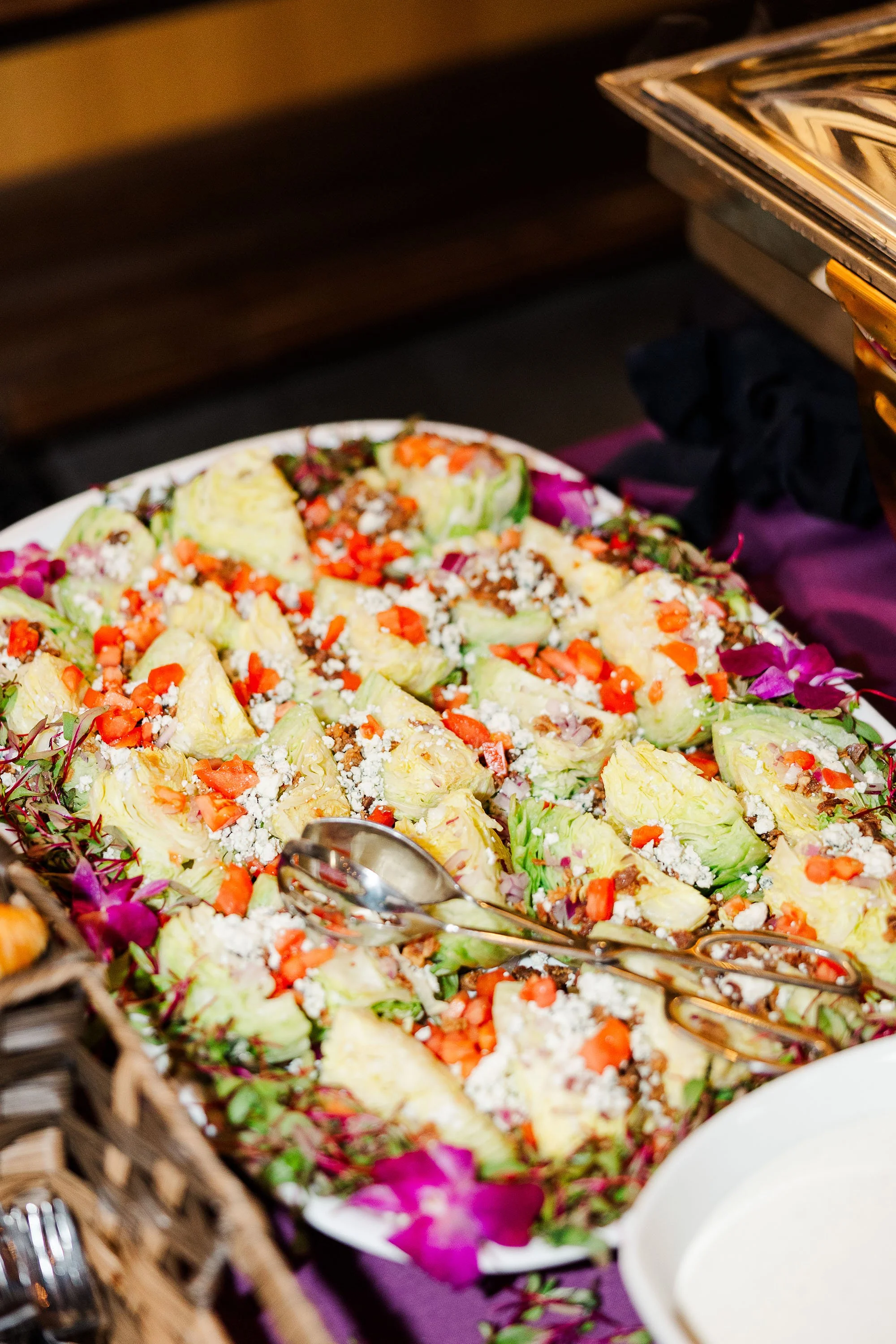 Salad with chopped lettuce, tomatoes, crumbled cheese, and garnishes on a platter at a buffet.