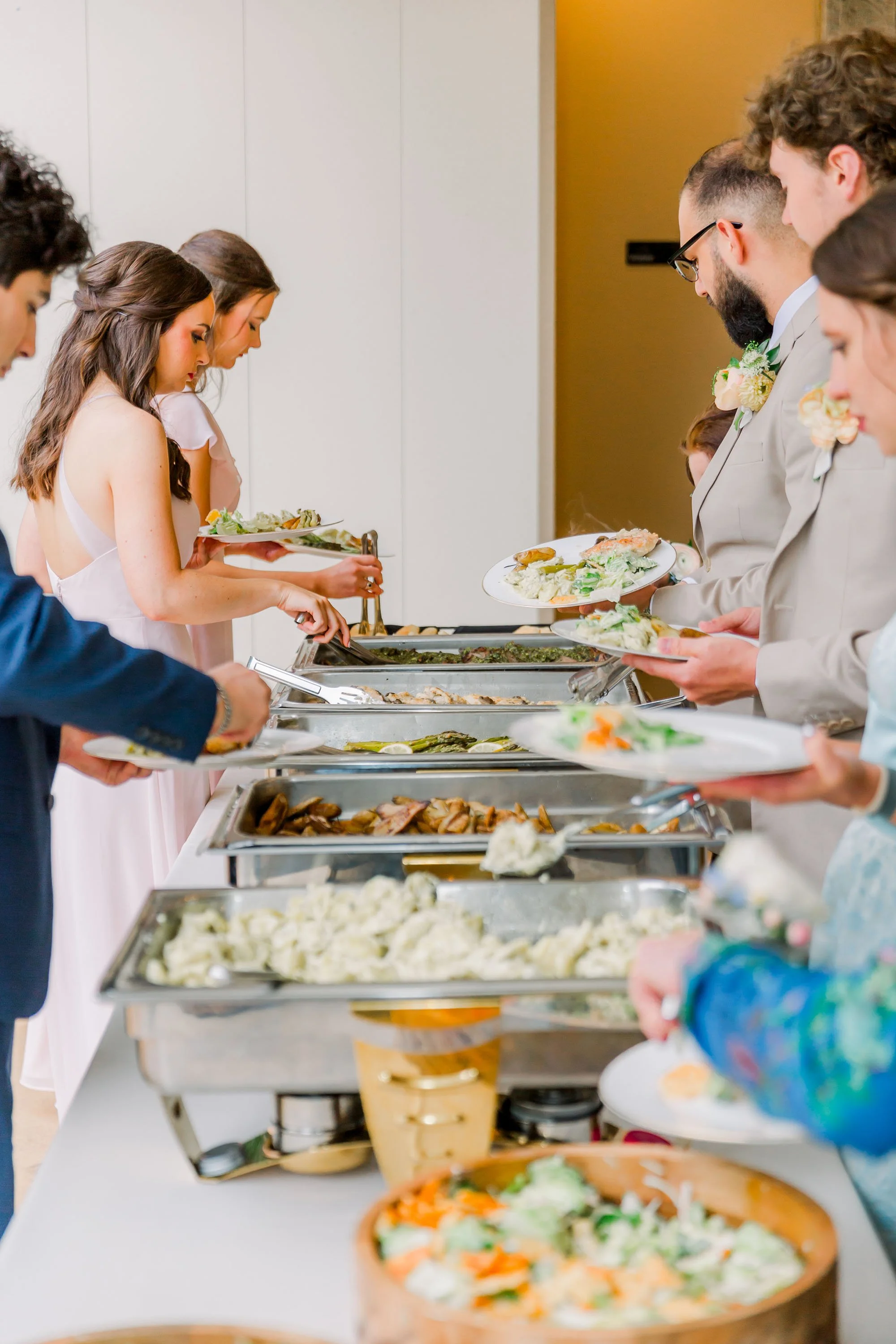 Guests serving themselves food at a buffet table during a wedding reception.