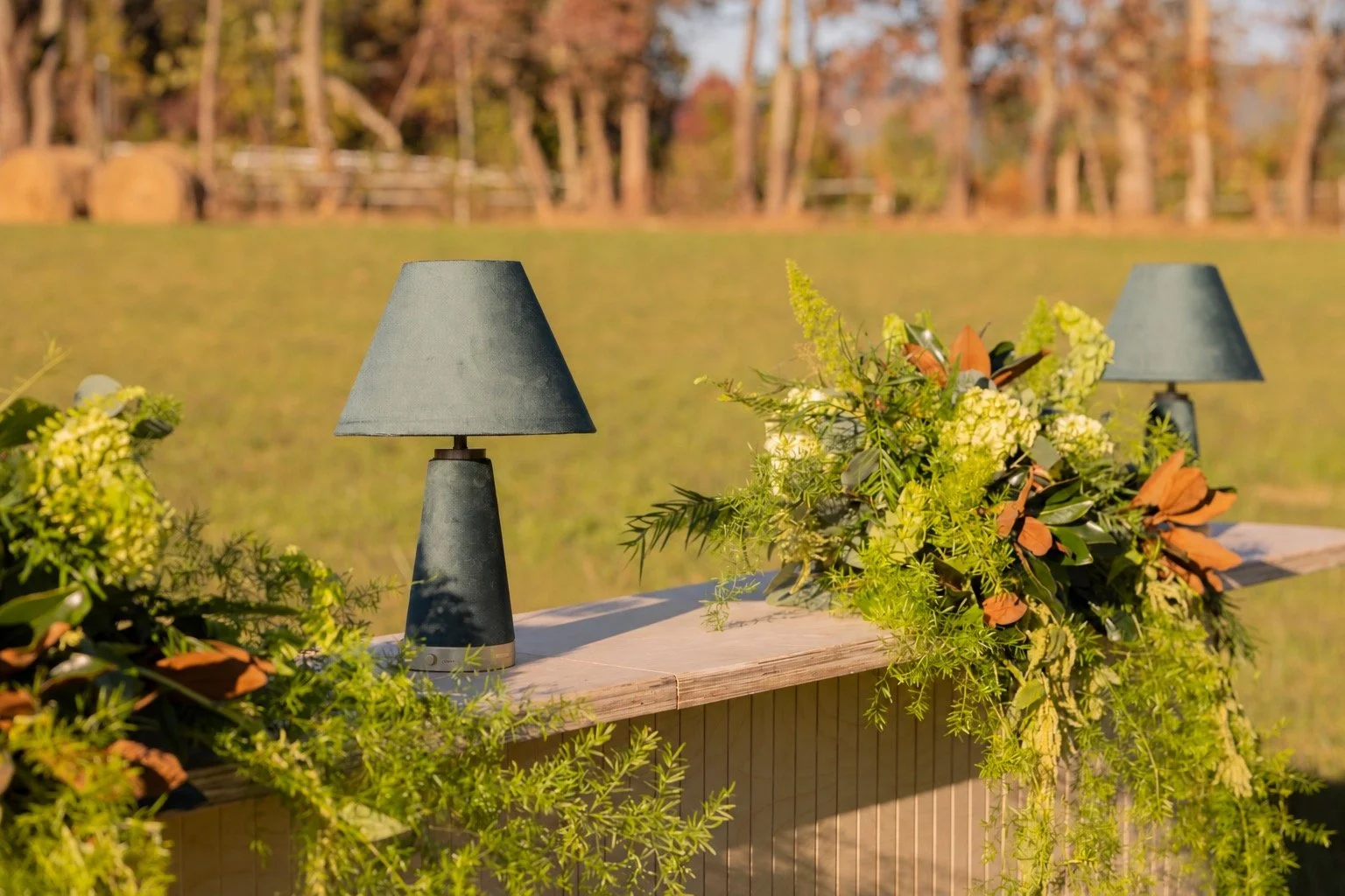 Outdoor fall wedding bar decorated with lush greenery, seasonal florals, and modern table lamps at The Lumigail near Gatlinburg, Tennessee.