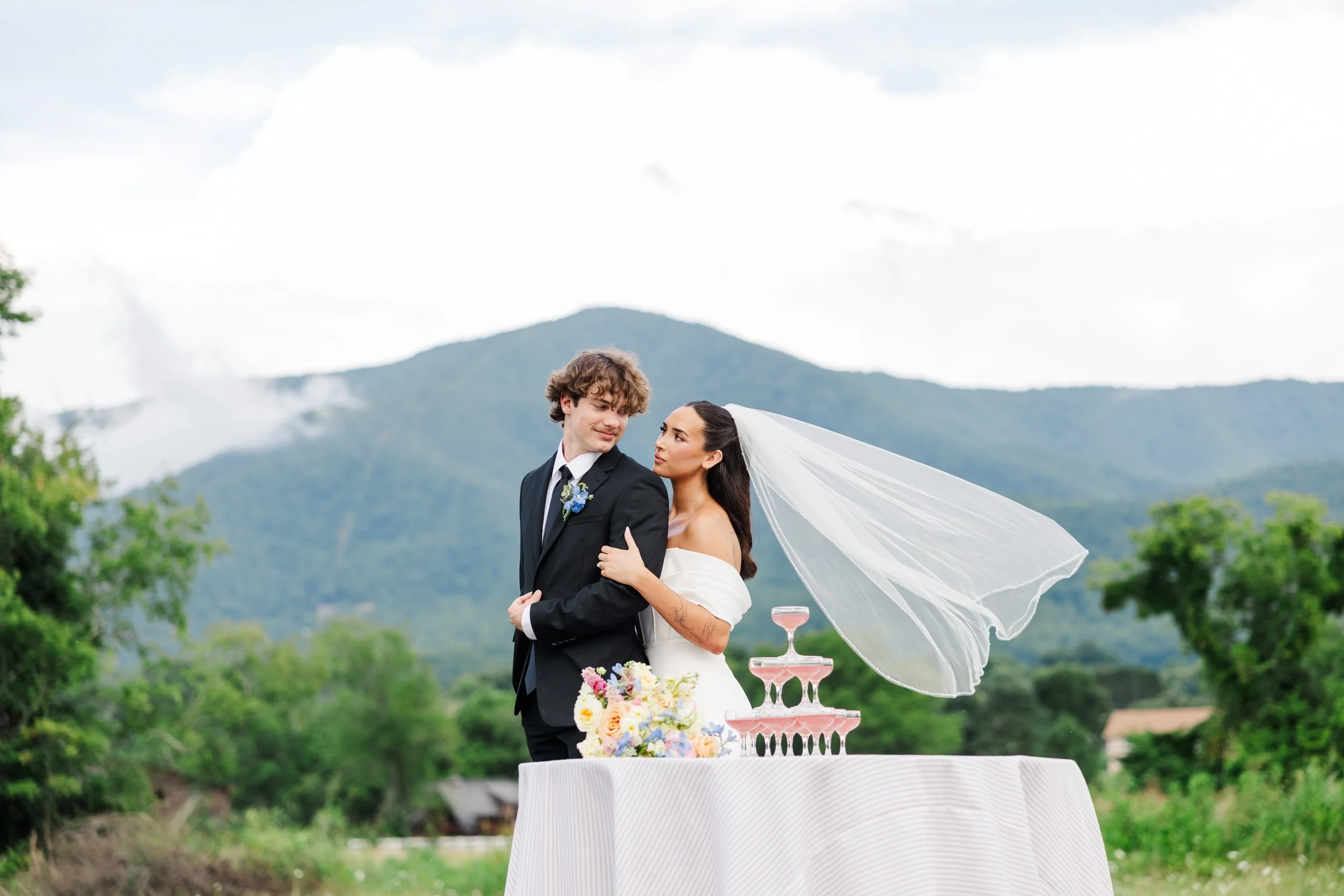 Bride and groom with a flowing veil, champagne tower, and Smoky Mountain views at The Lumigail wedding venue in Wears Valley, Tennessee.